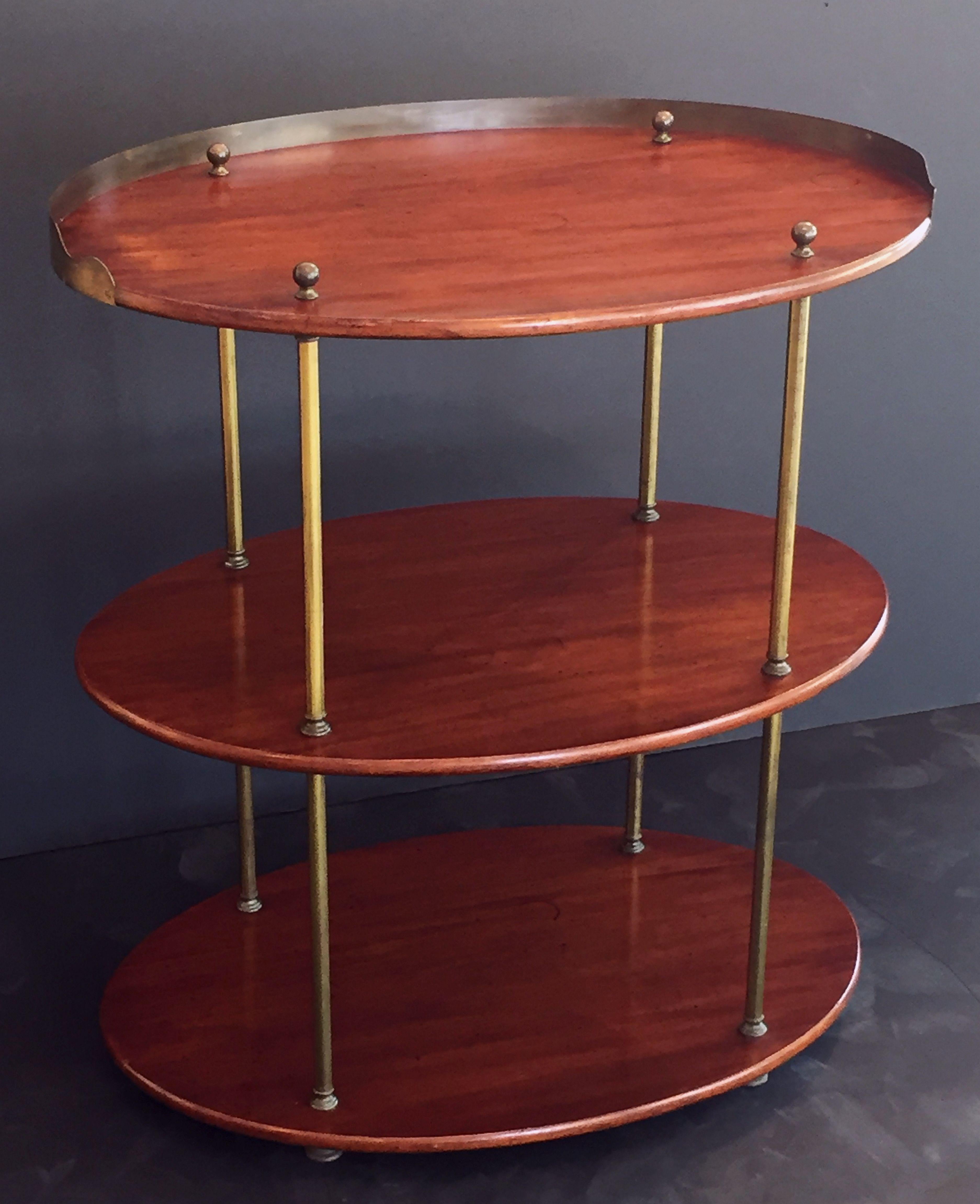 A Fine English Campaign ware or ship captain's table or three-tiered tray table of mahogany and brass, featuring an oval top with a brass gallery, over a middle and bottom tier, mounted by four stylish brass column posts, with round finial tops and