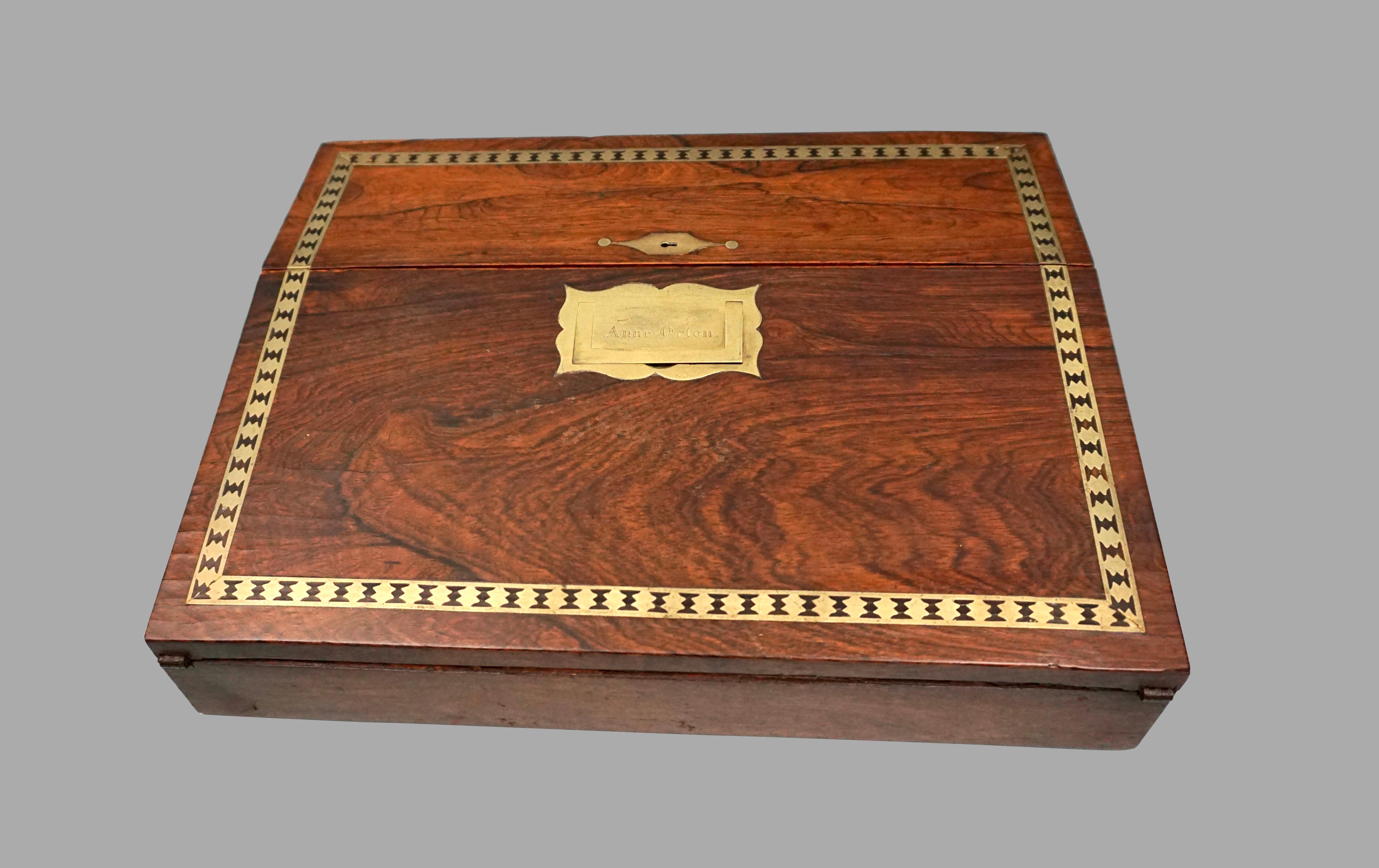 A fine quality brass inlaid Campaign style traveling desk with a recessed brass handle engraved with the name of its owner, Anne Orten. The piece opens to reveal a velvet lined writing surface and pen rest with spaces for 2 inkwells. This item is