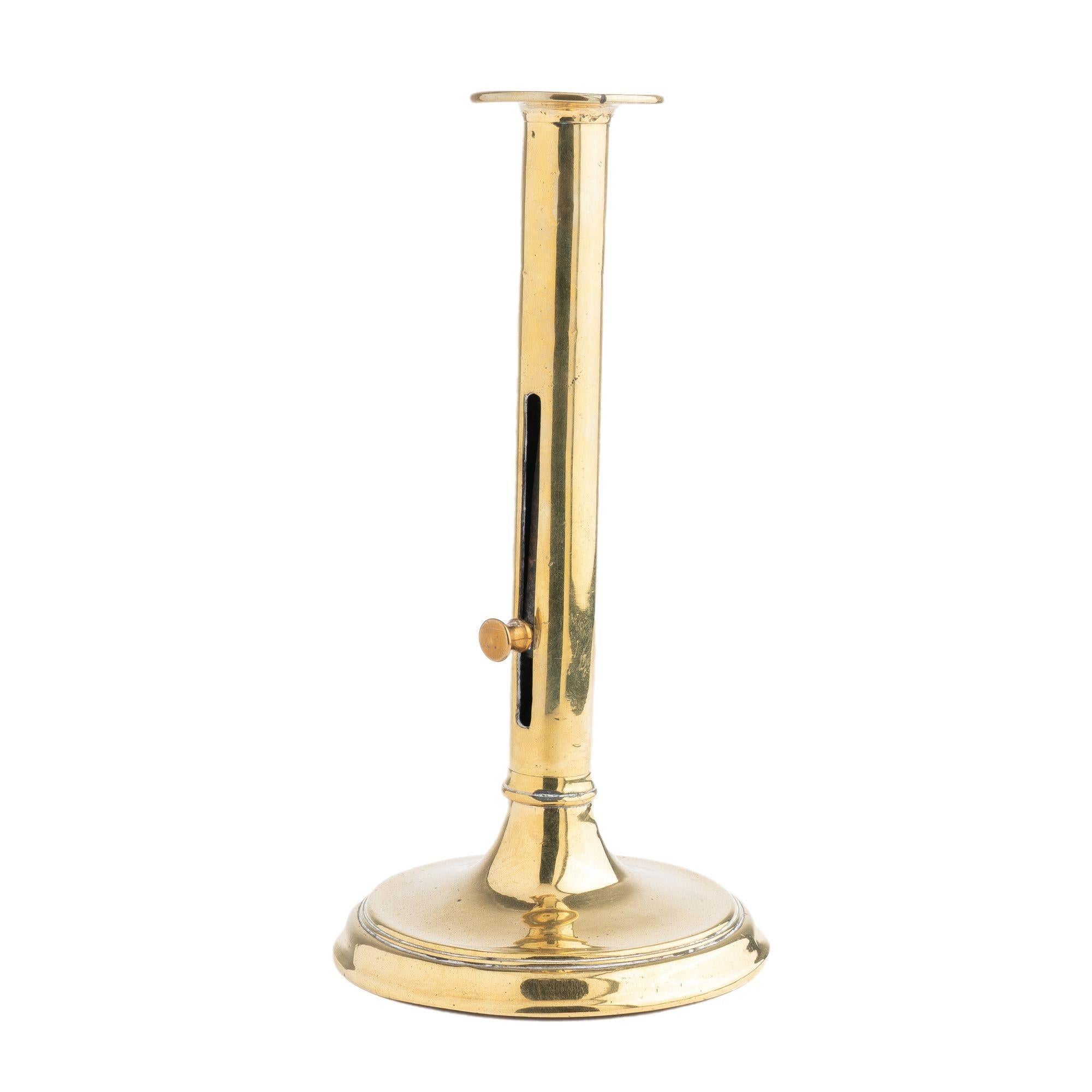 Cast brass cannon barrel candle stick with side, brass knob, and candle ejector. The cylinder shaft of the candlestick is peened to a raised circular base with dished drip pan detailed with a beaded rim.

England, circa 1820.