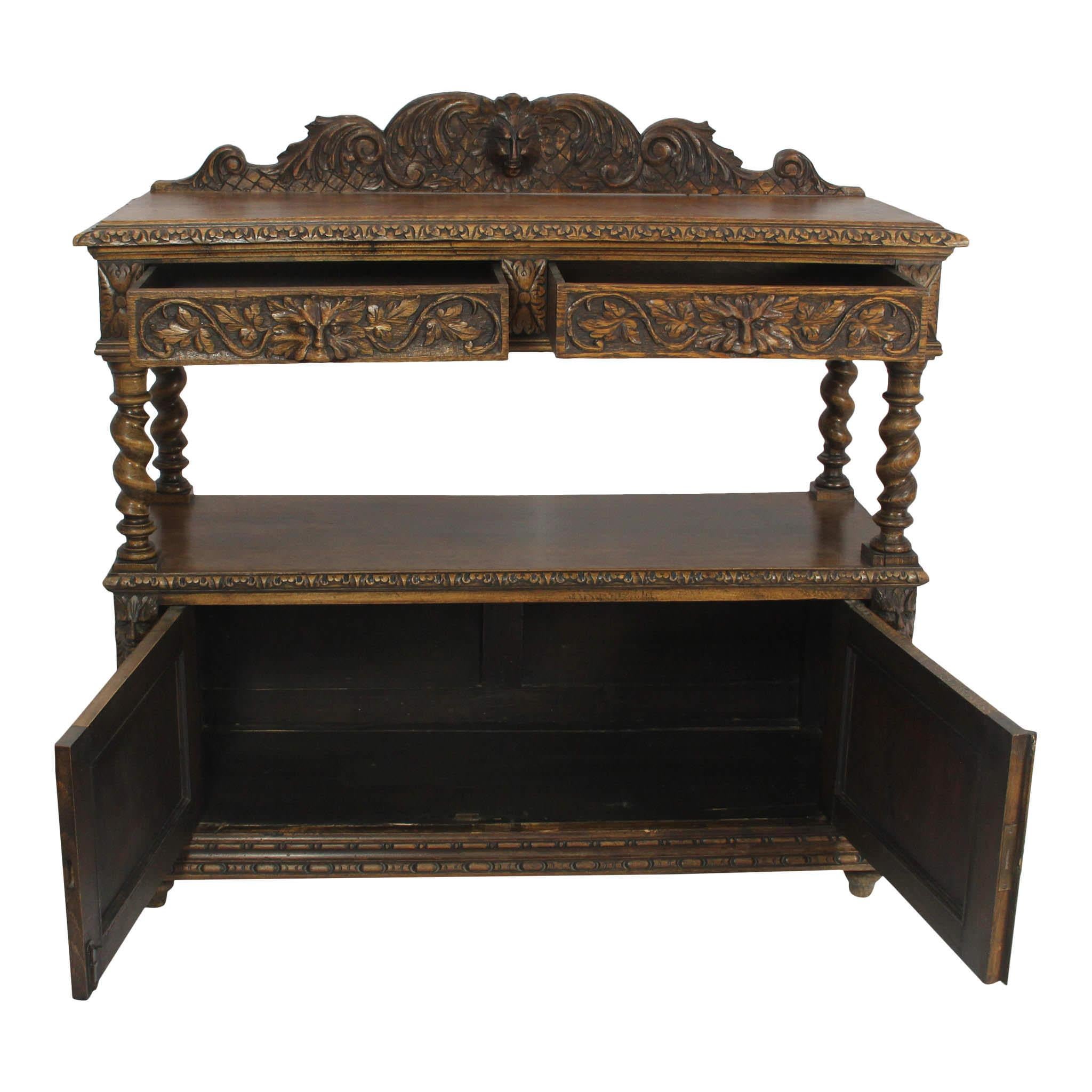 Five faces of the Green Man adorn this carved, oak buffet from England. Can you find them? The buffet has barley twist risers between the drawers and lower cabinet. Carvings of fruits and foliage grace the buffet doors.