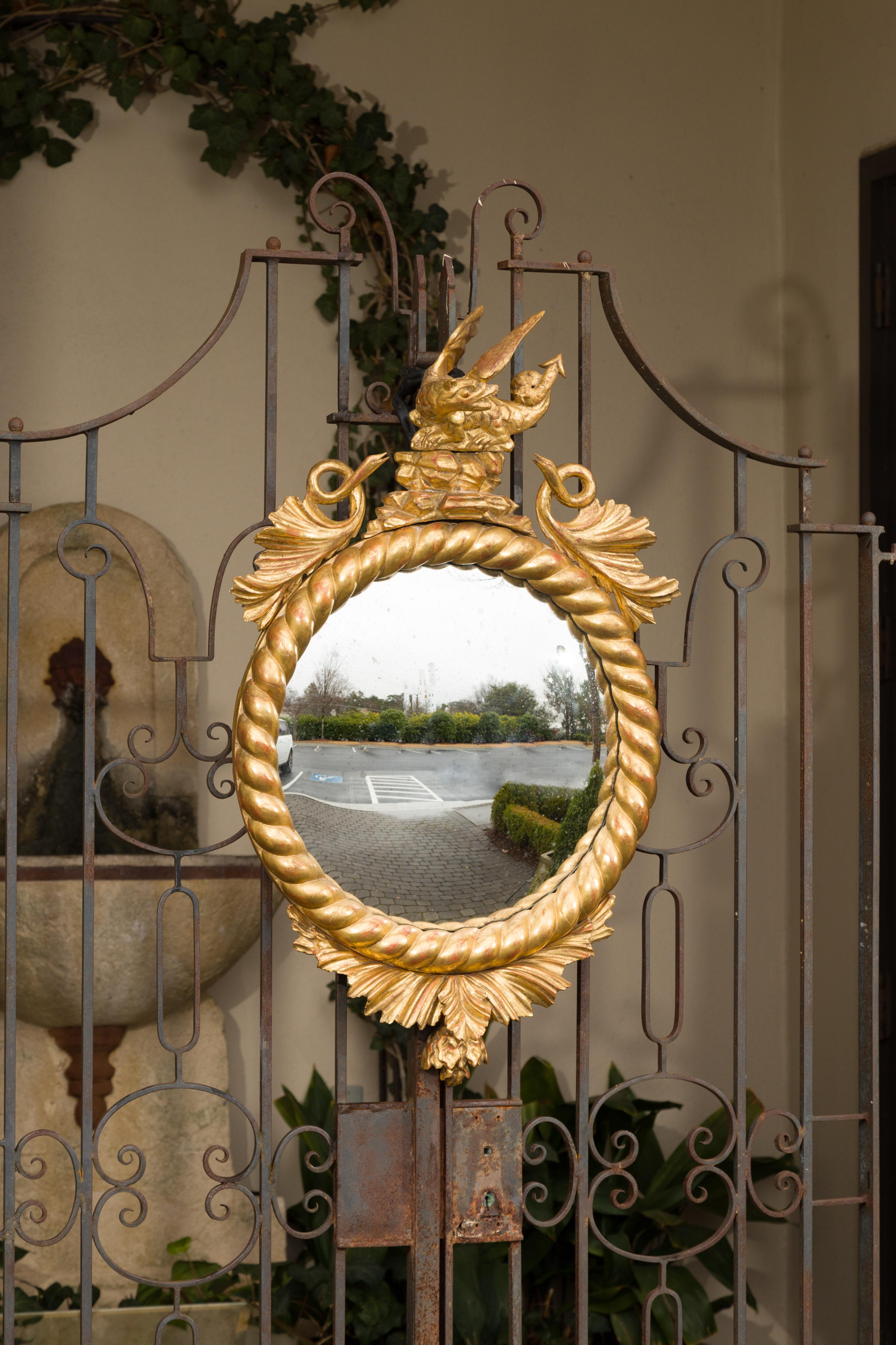 An English carved giltwood convex mirror from the 19th century, with mythical creatures and twisted frame. Born in England during the second quarter of the 19th century, this giltwood mirror captures our attention with its carved crest topped with a