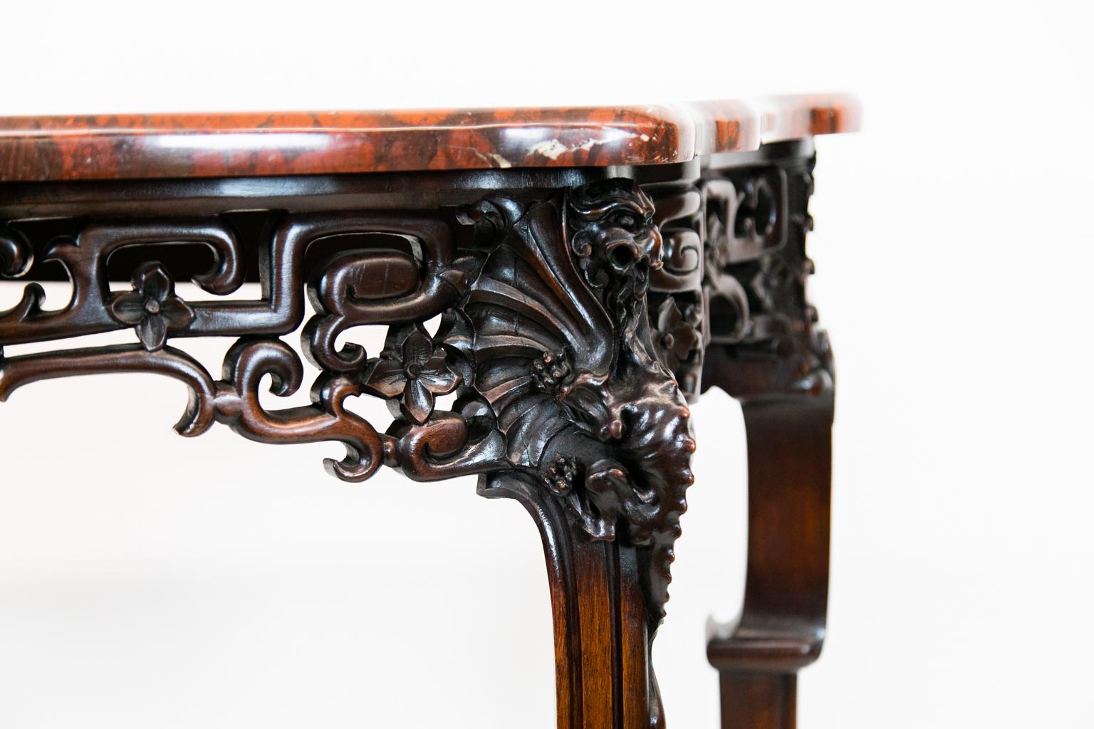 English carved marble-top console table has deep red marble with white figuring. The apron and sides are carved in a distinctive Chinese style but with English embellishments of carved masks. The lower section is joined with stretchers that join in