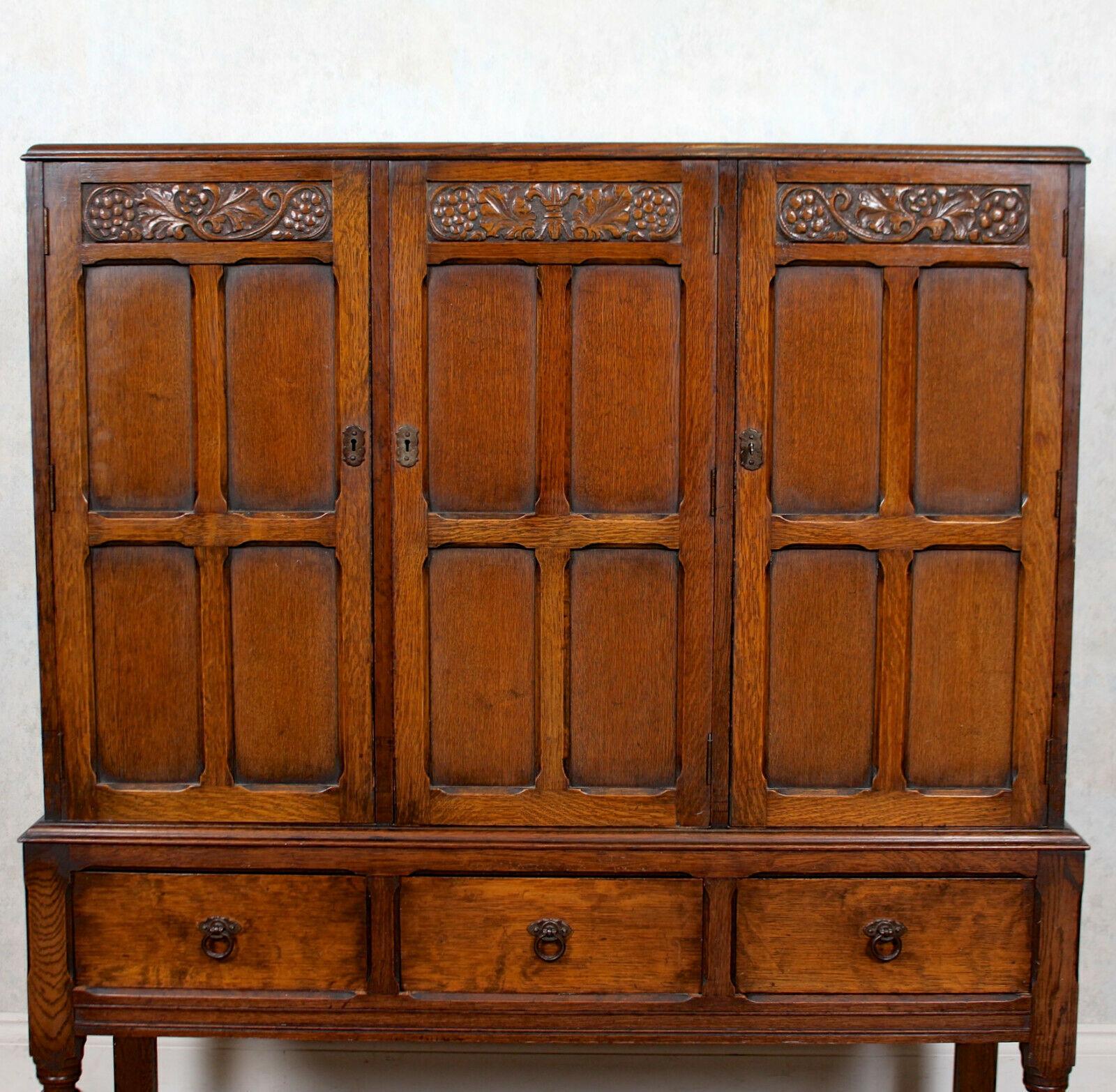 A fine quality carved oak cabinet.
Constructed from thick cuts of solid oak boasting a well figured grain and rich patina.
Three panelled doors bearing a carved leaf and berry design enclosed shelving above three short drawers raised on bulbous
