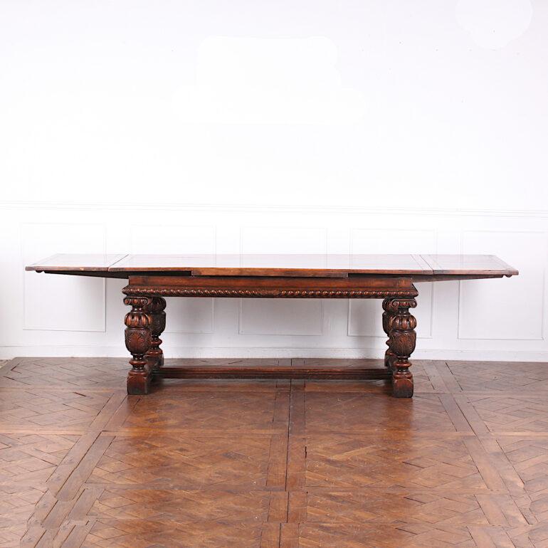 A long English carved oak ‘draw-leaf’ extending trestle table with a carved apron and thick turned legs united by and ‘H’ stretcher. A very sturdy table suitable for everyday use. Remains level and flat with one or two leaves pulled out. Dimensions