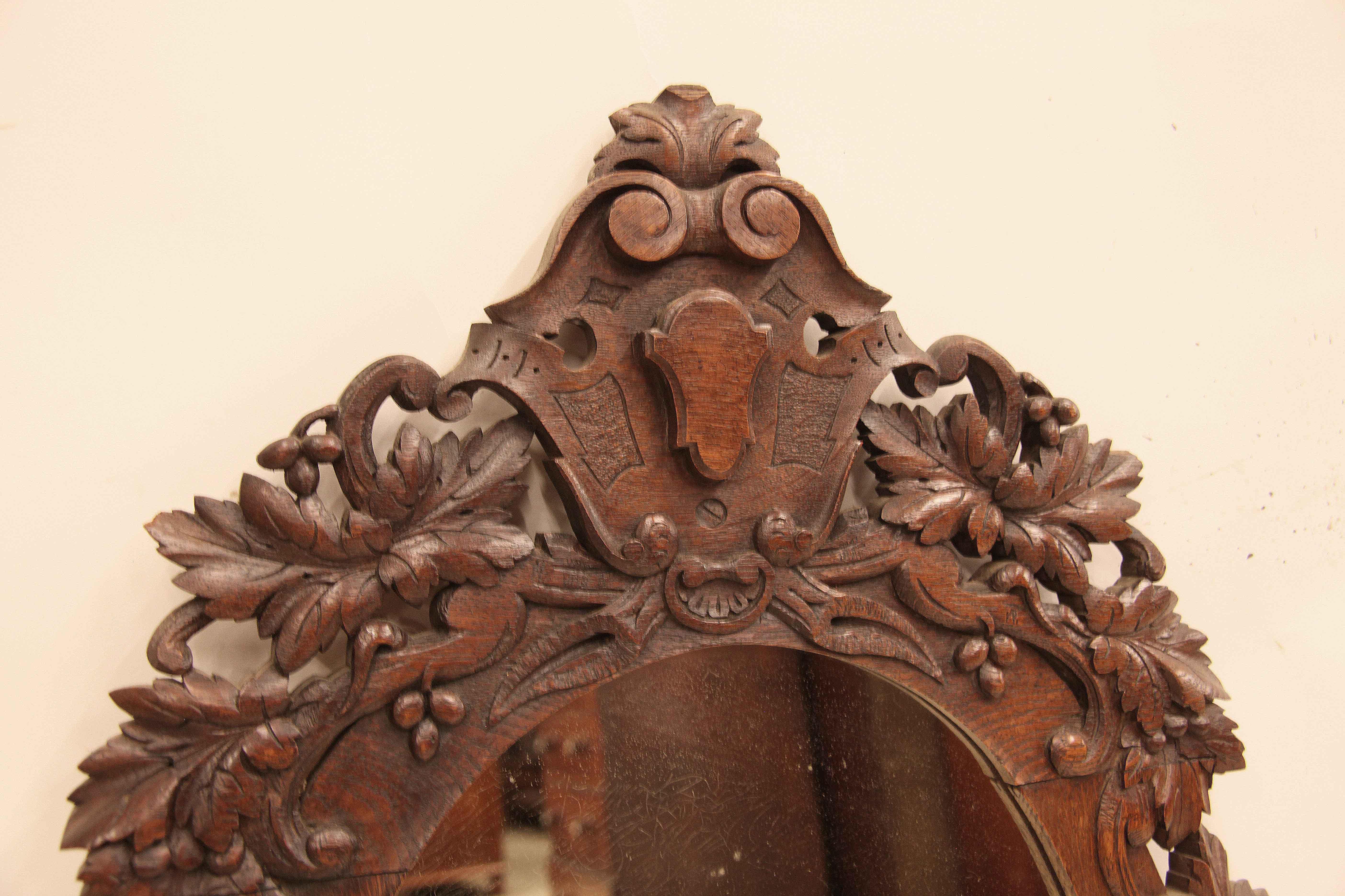 English carved oak oval mirror with carved shield at the top , the entire perimeter features leaf and grape carving in high relief connected with arabesques.  The mirror is original as well as the beautiful color and patina.