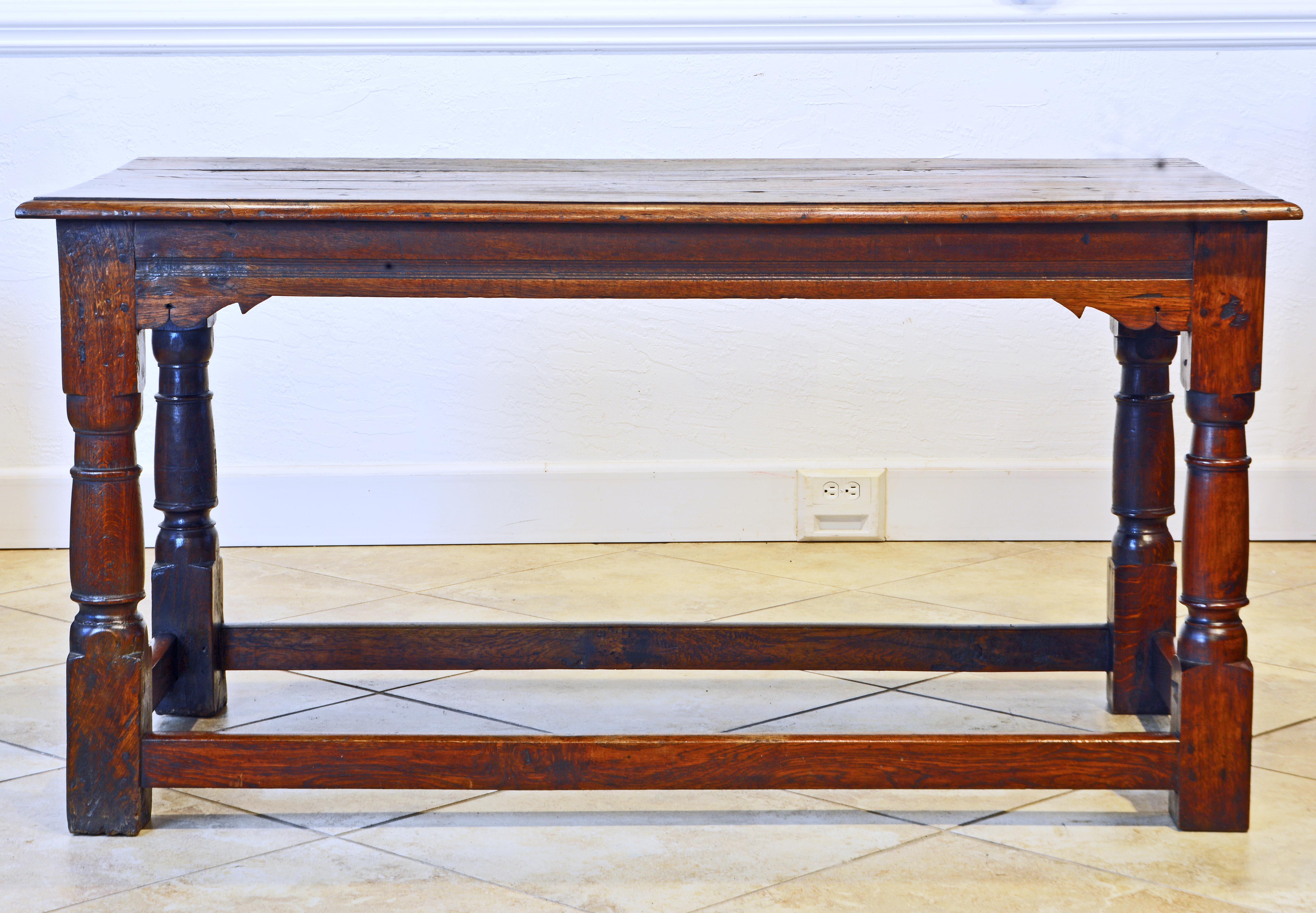 An exquisite 18th century English oak refectory table featuring a well patinated four plank top above a beautifully carved frieze with inlay of molded channel resting on four baluster carved legs joined by the stretcher base. With its beautiful warm