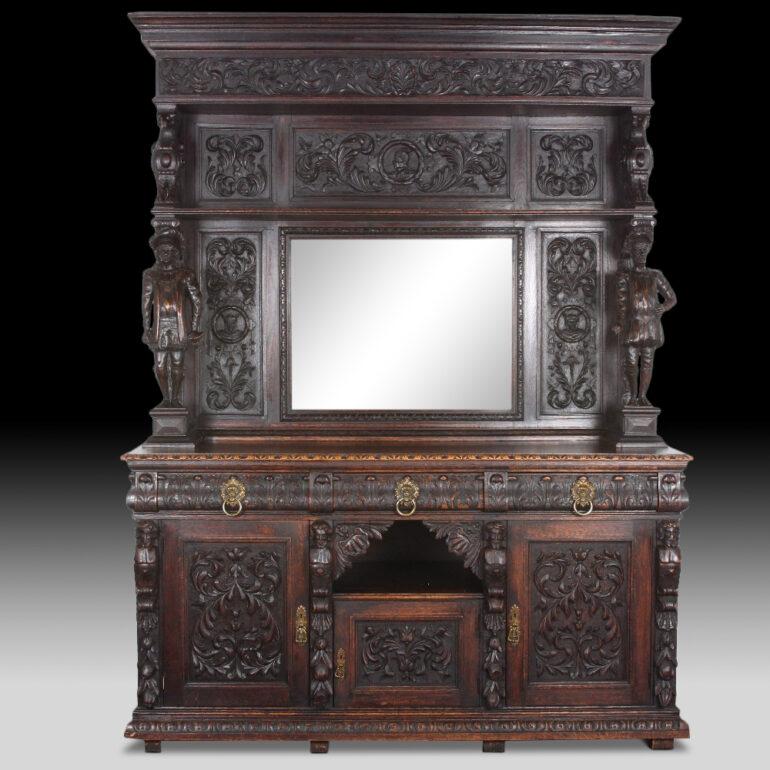 A profusely-carved Victorian solid oak buffet retaining the original dark patinated finish, the base with three carved-paneled doors below three drawers with brass lion’s head pulls, the ornate mirror back with carved faces and flora and scrolls