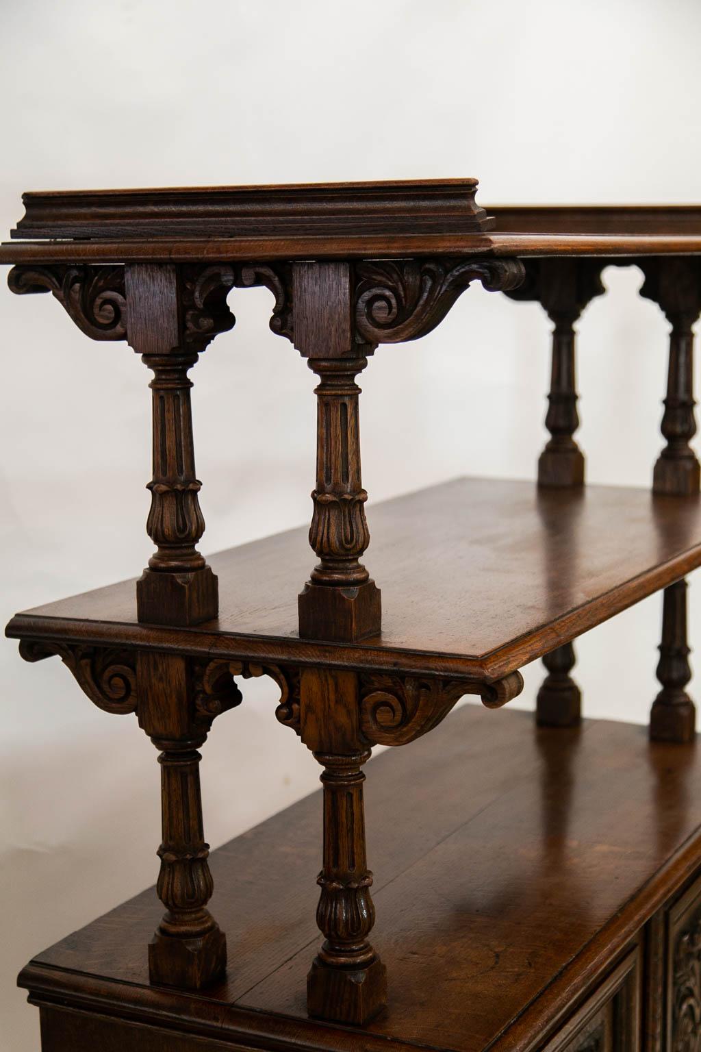 The top shelf of this three tiered server has a shaped molded gallery. The upper and middle shelf are supported by double fluted columns braced by carved arabesques. The lower doors have panels carved in high relief with fruit and floral arabesques.