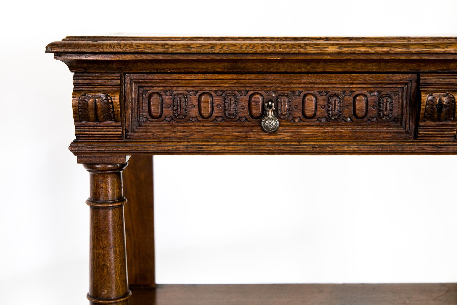 This English carved three-tiered server has two drawers that have carved drawer fronts that are separated and flanked on either side with stylized carved leaves. The top lifts to reveal a marble inset working surface and a fold down shelf supported