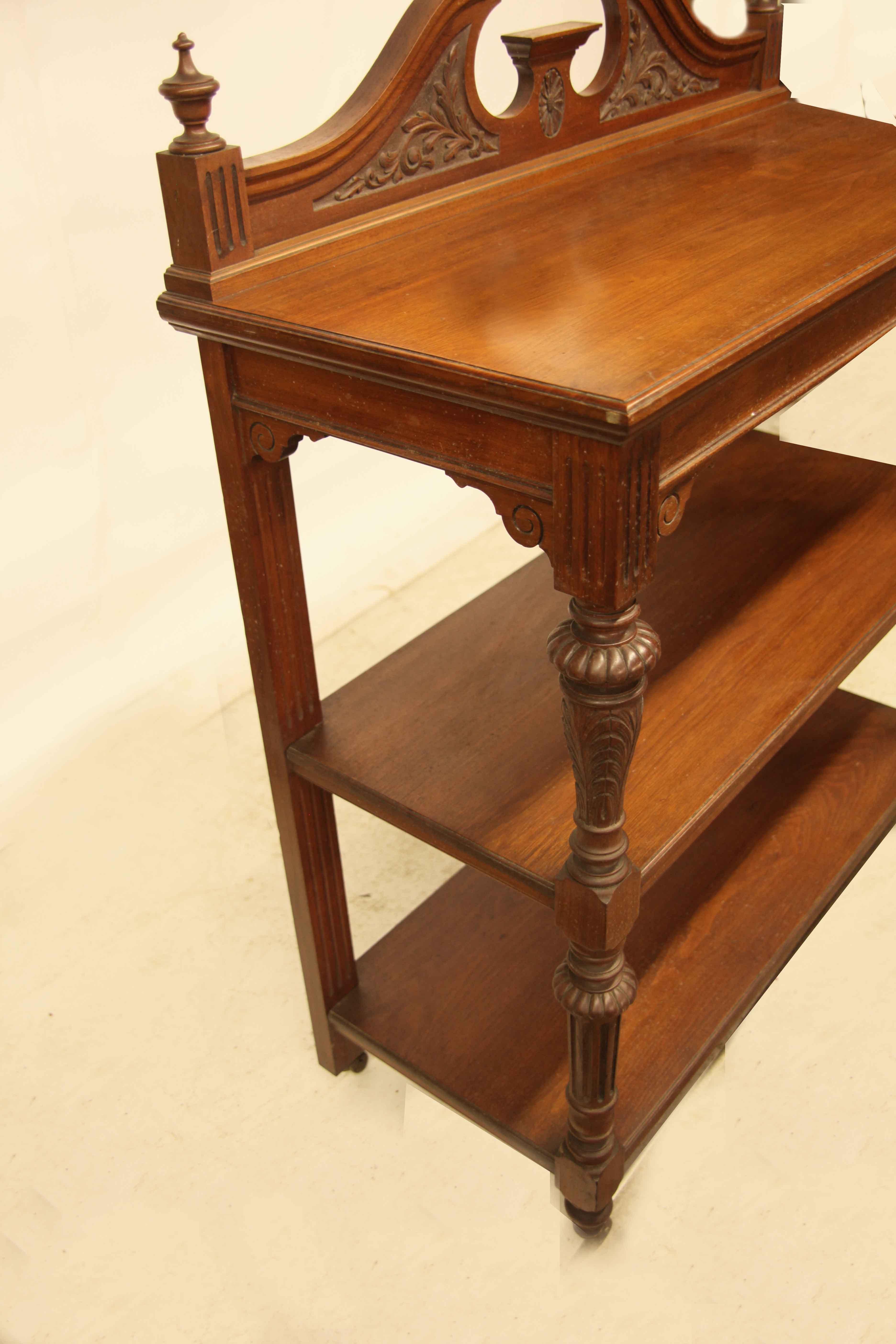 English carved walnut three tier server, the gallery along the back with carved foliate in the broken arch and carved oval medallion in the center, turned finials on each end. The three tiers are supported in the front by intricately carved baluster