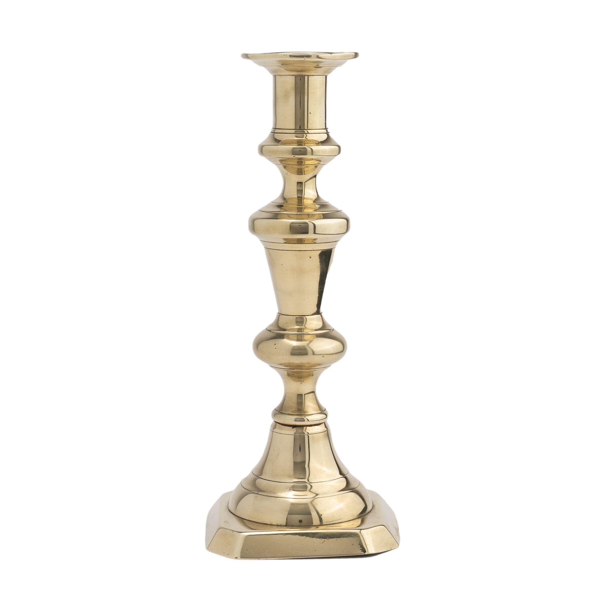 Bold cast brass baluster candlestick with cup and bobeshe. The candle shaft is fitted with an internal push up candle ejector and the candle shaft is peened to a raised square base with cut corners.

Birmingham, England, circa 1830.