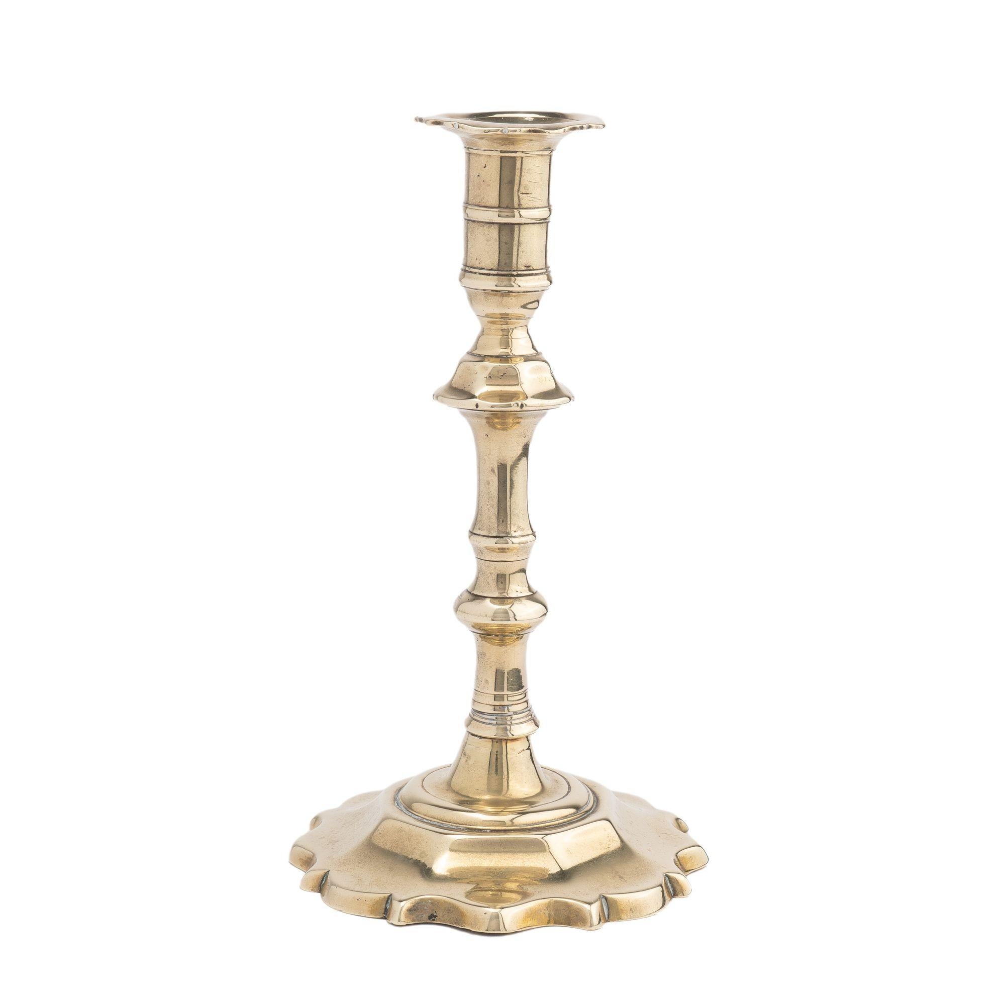 Queen Anne hollow core cast brass candlestick with scalloped edge bobeche and a faceted shaft knob peened to a scalloped edge domed base. A square groove on the interior of the candle cup indicated that is once had an internal screw candle ejector