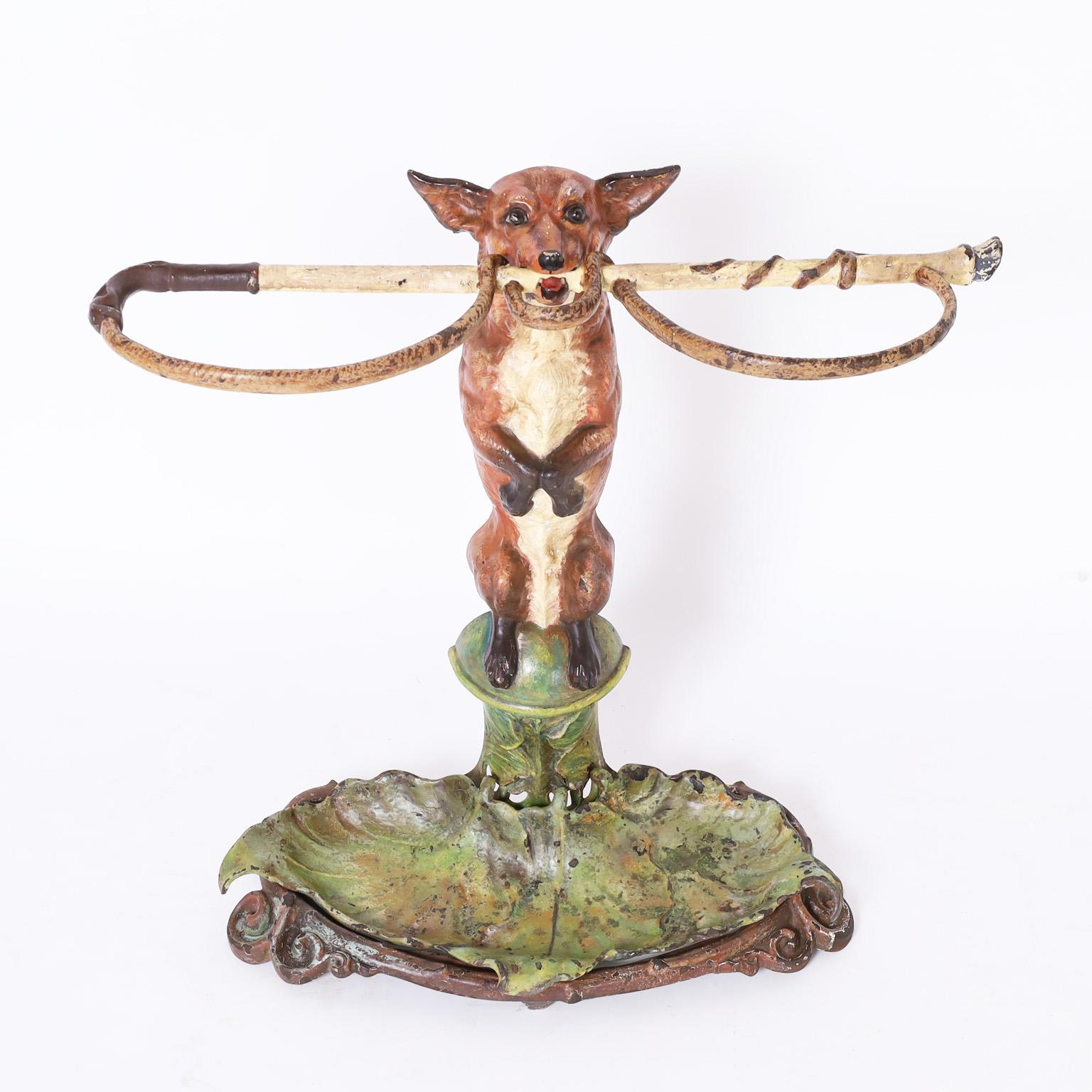 Outfoxed by a 19th century English cast iron umbrella stand, retaining its original paint, of a fox holding in its teeth a hunting whip or crop over a removable leaf form water tray.