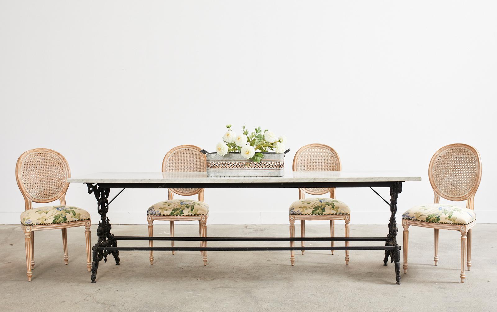 Fantastic English Gothic revival cast iron patio and garden dining table or console table featuring a one inch thick slab of Italian Carrara marble. The cast iron base is made in a trestle style with hourglass form legs on each end decorated with