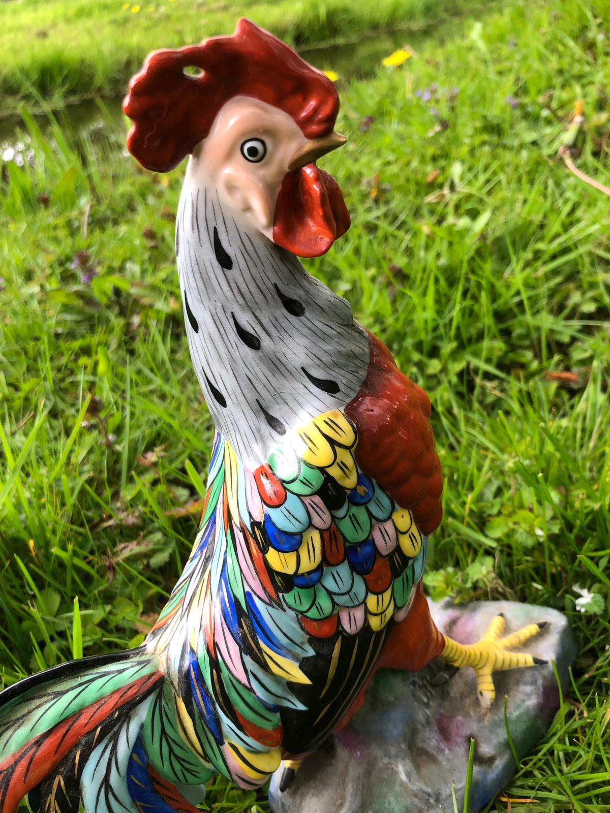Porcelain colorful rooster by Chelsea House marked with the gold anchor. Manufactured in England, the rooster is perched on a branch and features tones of red, grey, yellow, blue, green and black. The rock is the stone on which the rooster is