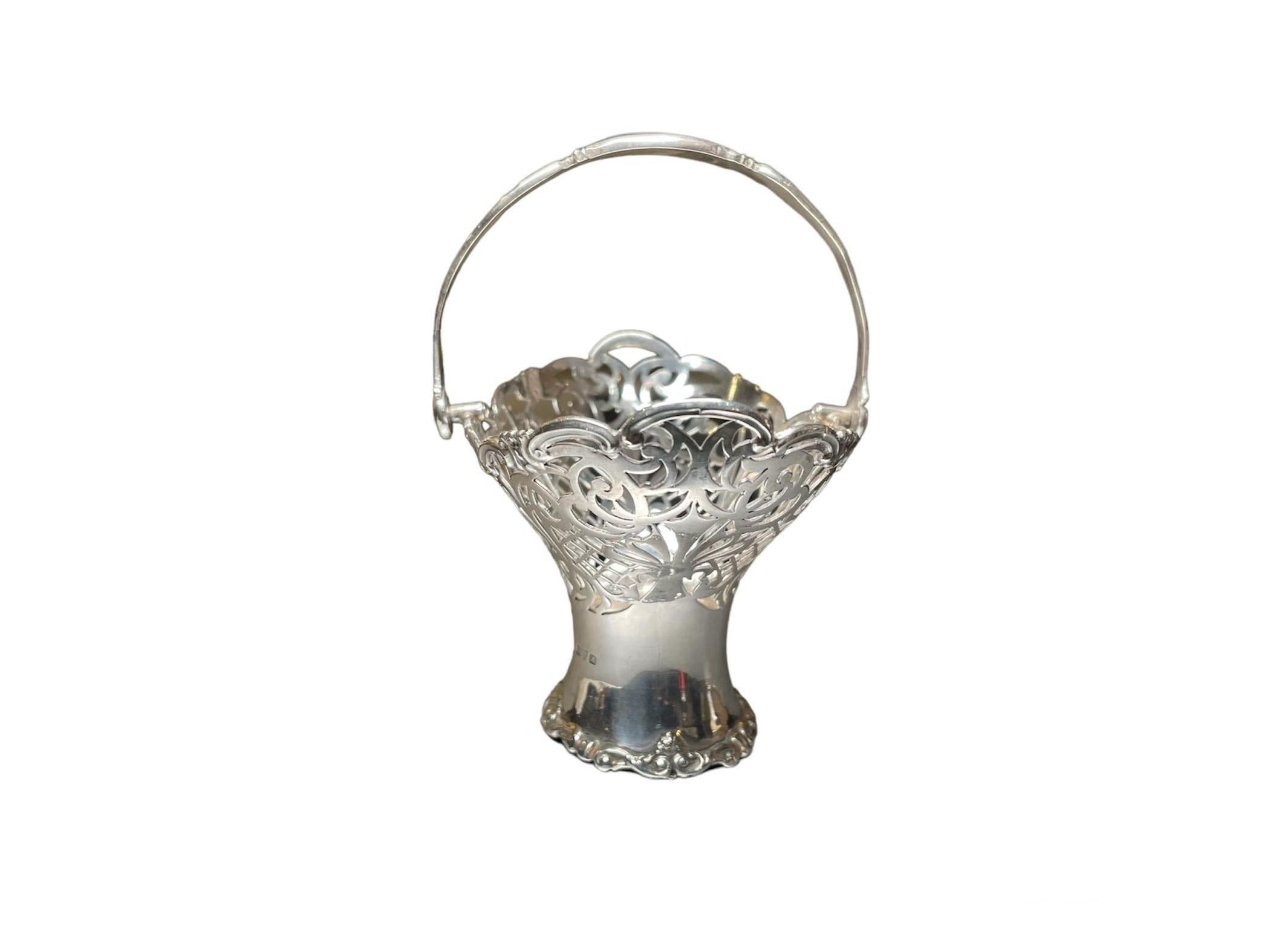 This is an English Chester Sterling Silver Bon Bon/ Nuts Basket. It depicts a  wide “V” shaped basket with scalloped border and pierced walls decorated with scrolls and “laces”. It has also a sterling swing handle. The basket has the English Chester