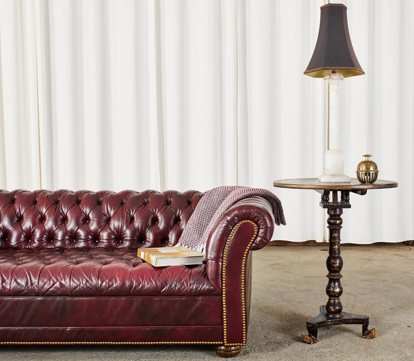 Classic English chesterfield sofa settee featuring an oxblood or cordovan tufted leather upholstery. The frame was crafted with large English rolled arms having a tufted leather seat, arms, and back. The front of the sofa has brass tack nail head
