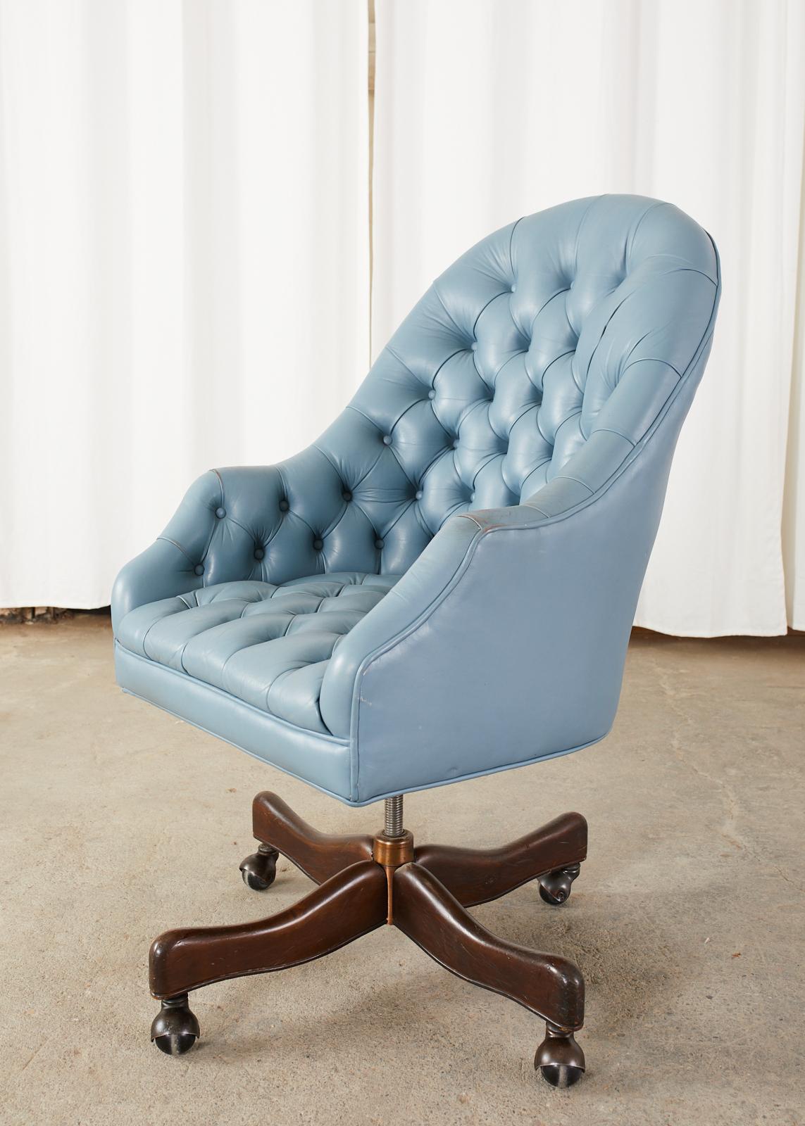 Fabulous mid-century executive office swivel desk chair featuring attractive French blue leather upholstery. Made in the English chesterfield style with a button tufted seat and back. Supported by an adjustable column conjoined to four mahogany legs