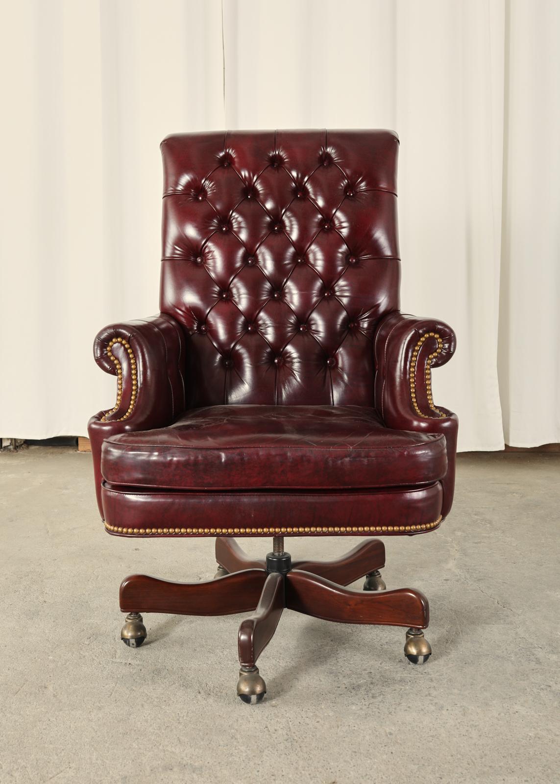 Stately executive office desk armchair made in the English chesterfield or regency style. The chair features a soft leather upholstery with a tufted back finished in a rich cordovan or oxblood red shade with a subtly marbled detail. The seat has