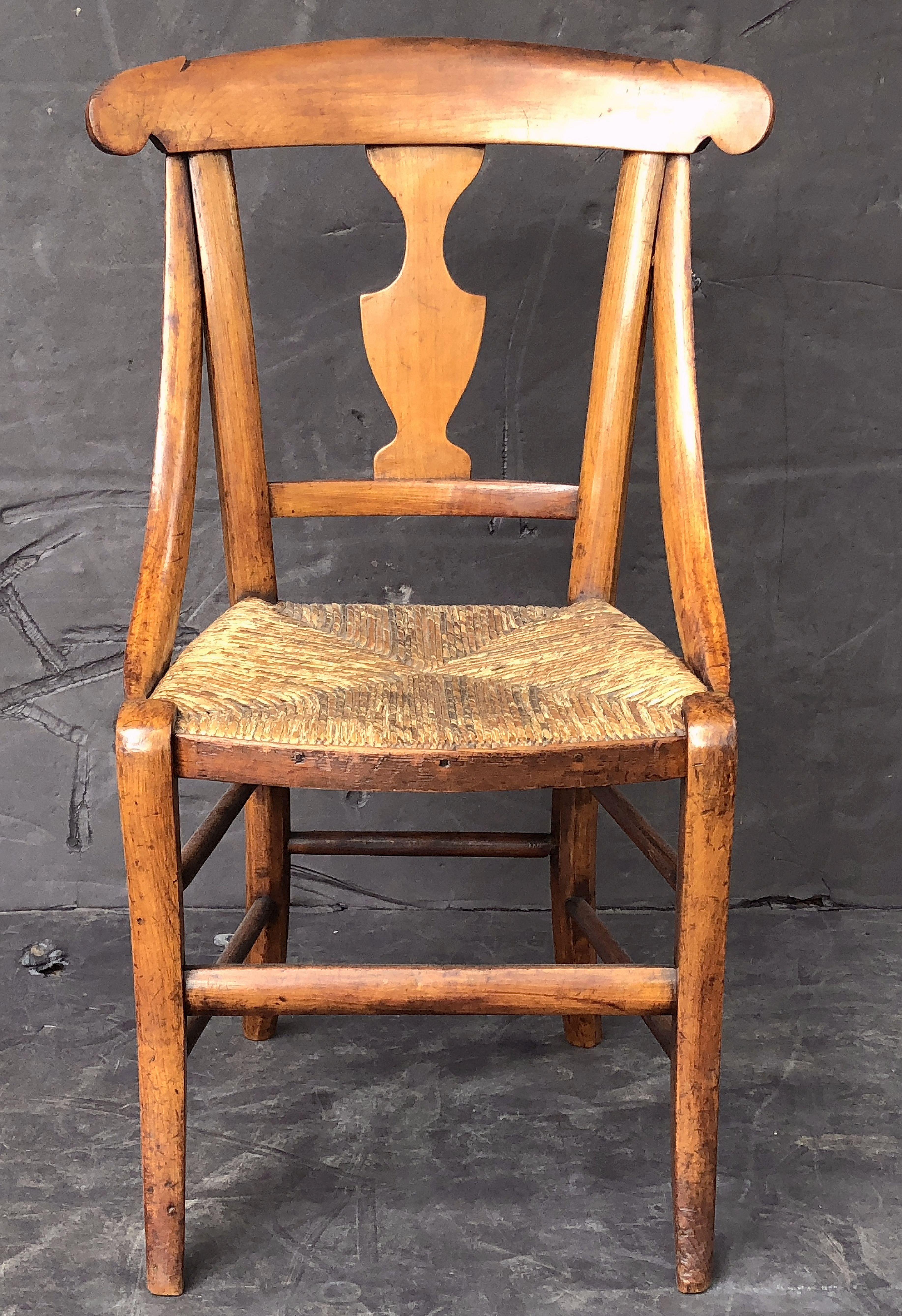 A fine English child's chair from the 19th century, featuring a handsomely patinated fruitwood frame with splat back and rush seat.