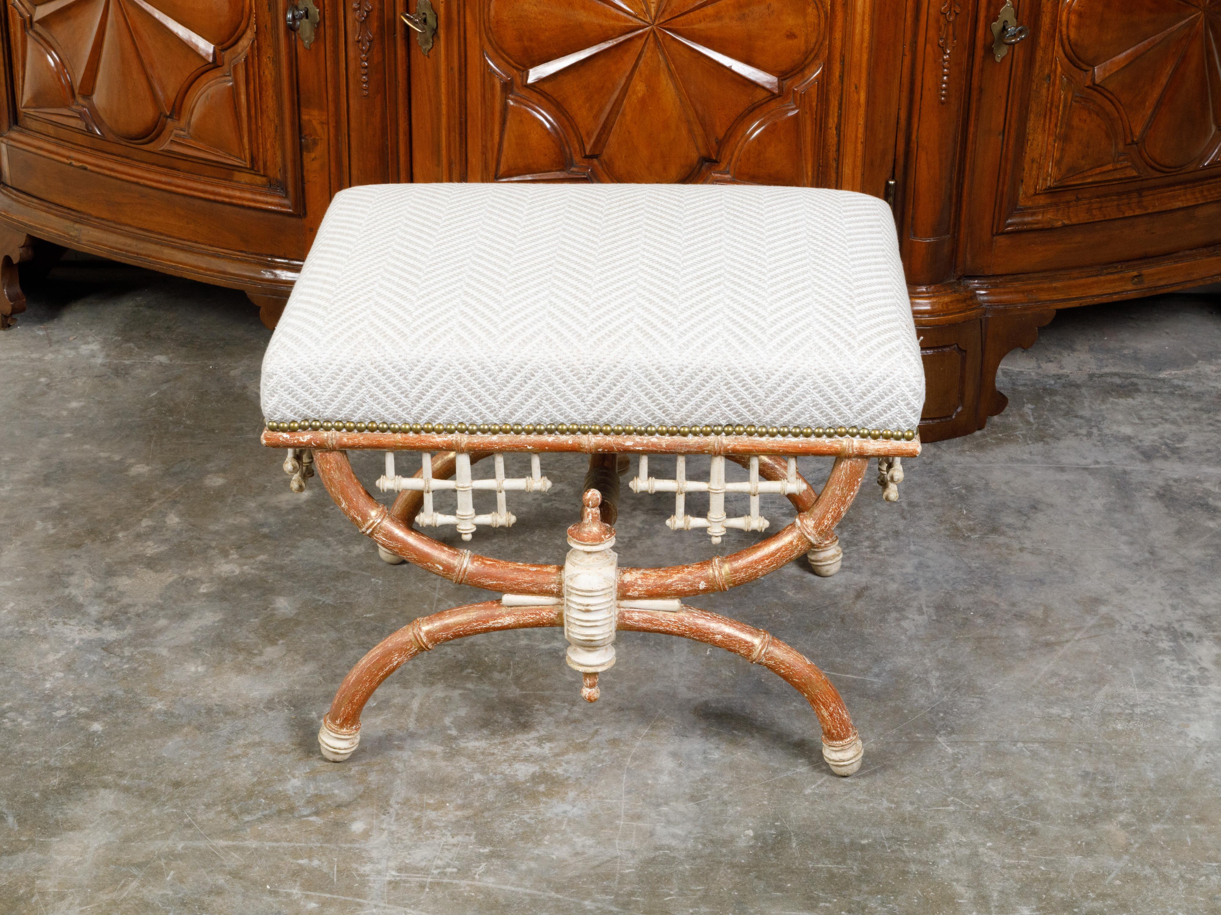 An English Chinese Chippendale style faux bamboo stool with X-Form base and new upholstery. Created in England, this stool features a rectangular upholstered seat secured with a brass nailhead trim, resting above Chinese Chippendale style motifs