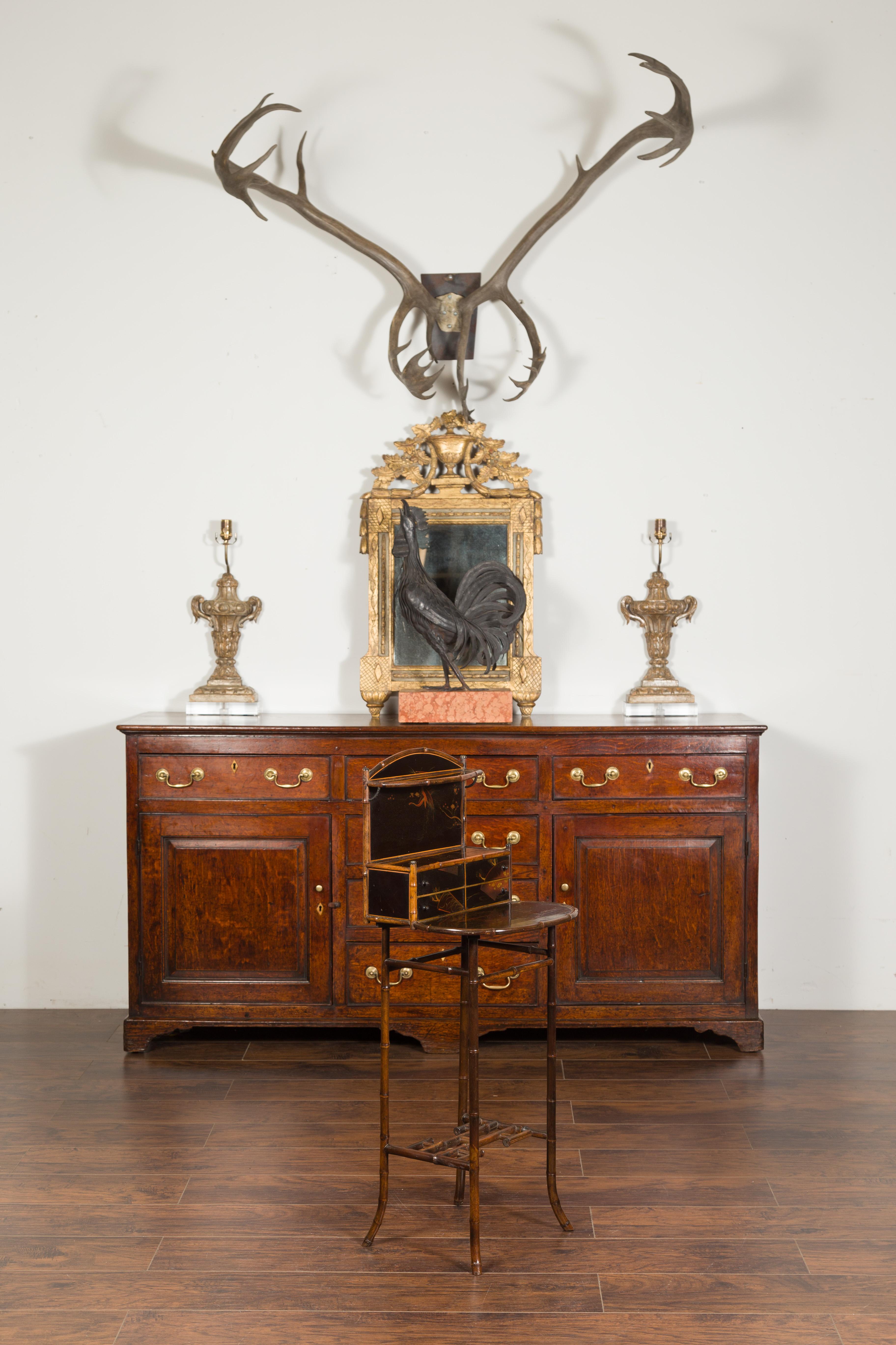 An English freestanding bamboo shelf from the early 20th century, with black Chinoiserie decor, drawers and intricate stretcher. Created in England during the early years of the 20th century, this freestanding shelf features a bamboo structure