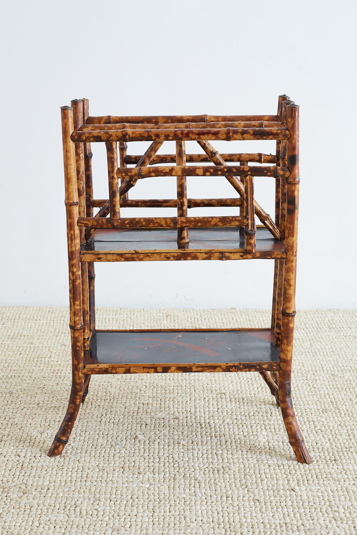 Large English bamboo Canterbury or magazine stand made in the chinoiserie revival taste of the early 20th century, Europe. Features a lovely lacquered tortoise shell finish with two painted tiers or shelves. The shelves have an Asian foliate motif.