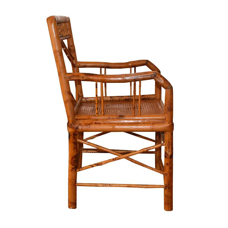 A delicate chinoiserie burnt bamboo or tortoise bamboo armchair. Fashioned from bamboo, the back features geometric shapes and lines. the arms are geometric as well, each with four pencil reed decorative bamboo pieces. On the front, the skirt is