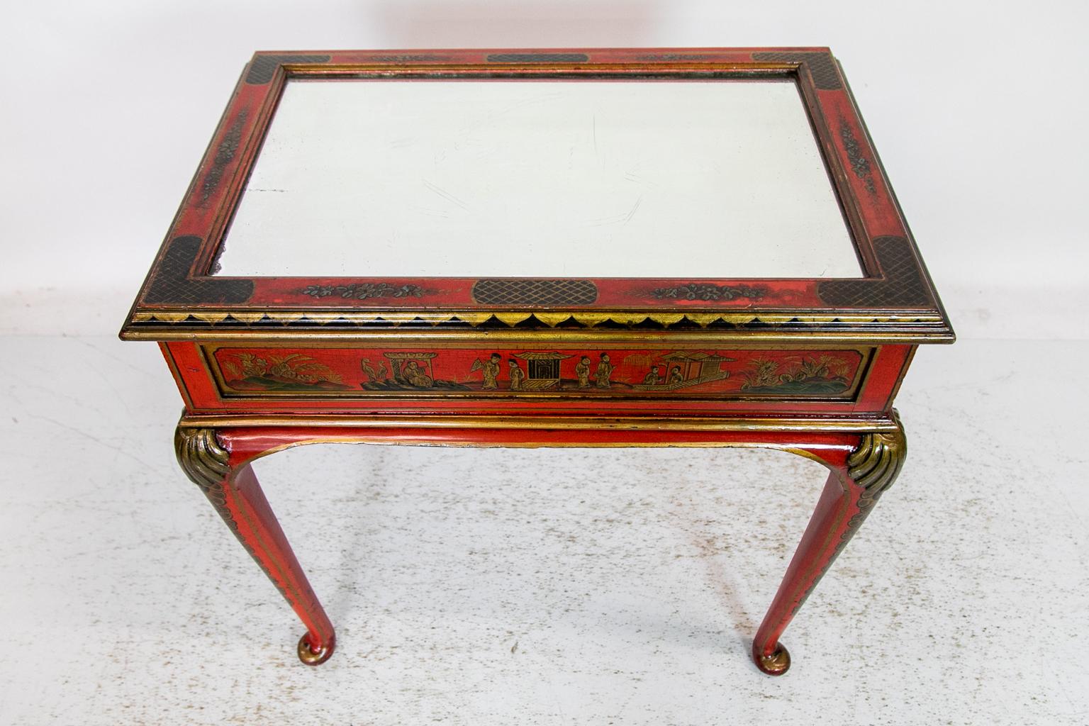 This English table is painted overall with chinoiserie decoration on a red background. The top has a mirrored center framed with gold and black floral and diapering motifs. The table is finished on all four sides, but the chinoiserie decoration is