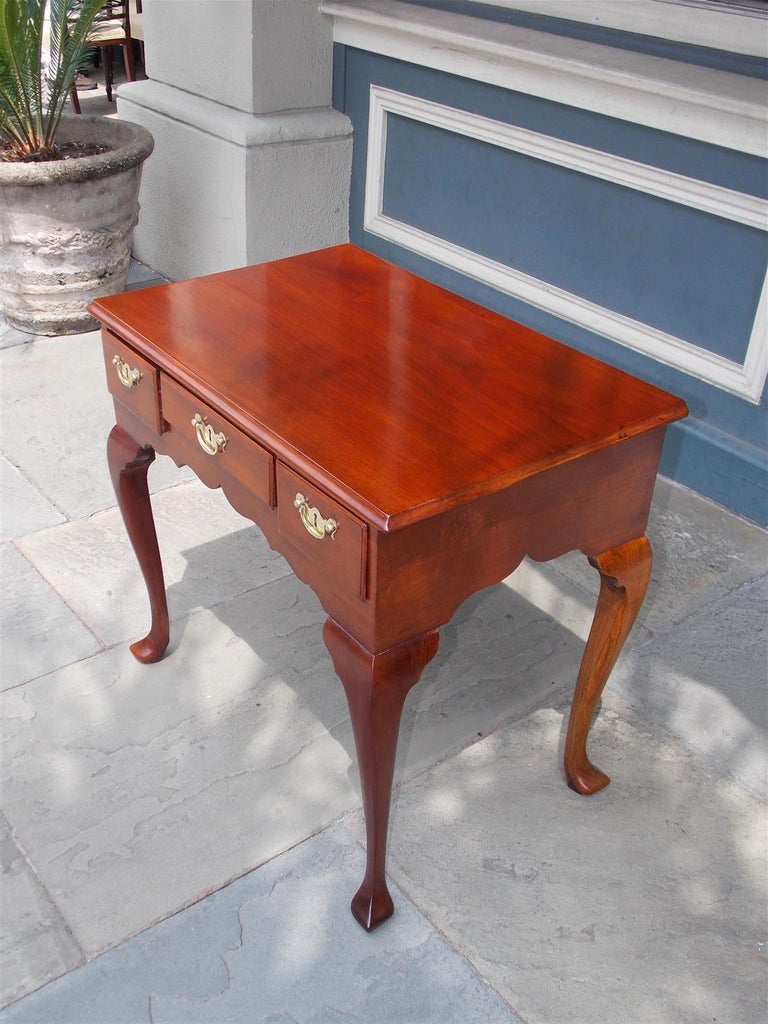 English Chippendale mahogany and walnut lowboy with a carved molded edge top, centered drawer with flanking side drawers, original brasses, carved scalloped skirt, exposed rear dovetails, and resting on carved knees with stylized pad feet, Late 18th
