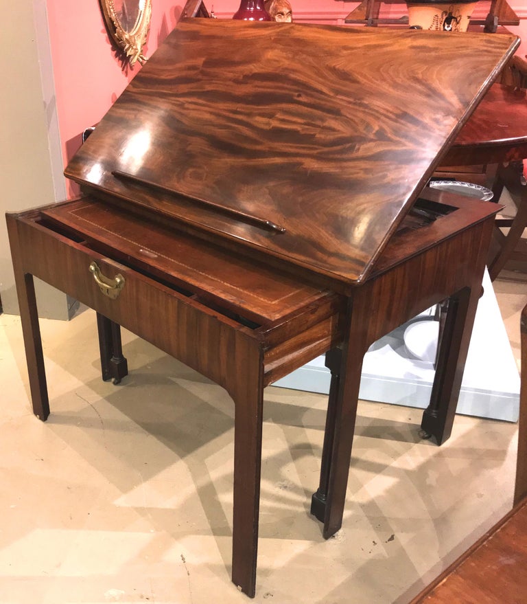 A wonderful English Chippendale crotched mahogany architect’s desk or design table with adjustable rectangular top that raises from a flat position to an elevated standing position, with wooden supports and a removable paper rest, surmounting a