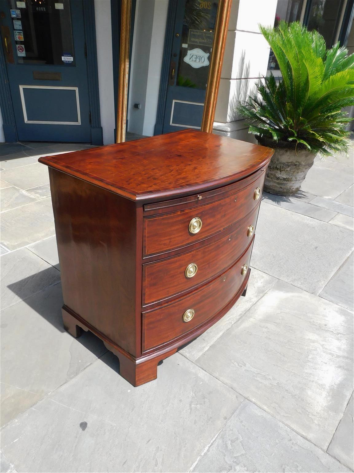 English Chippendale Mahogany bow front chest with three graduated drawers,  baize brushing slide with original brass pulls, satinwood string inlays, tulip wood cross banding, original brasses and interior locks, and resting on the original ogee