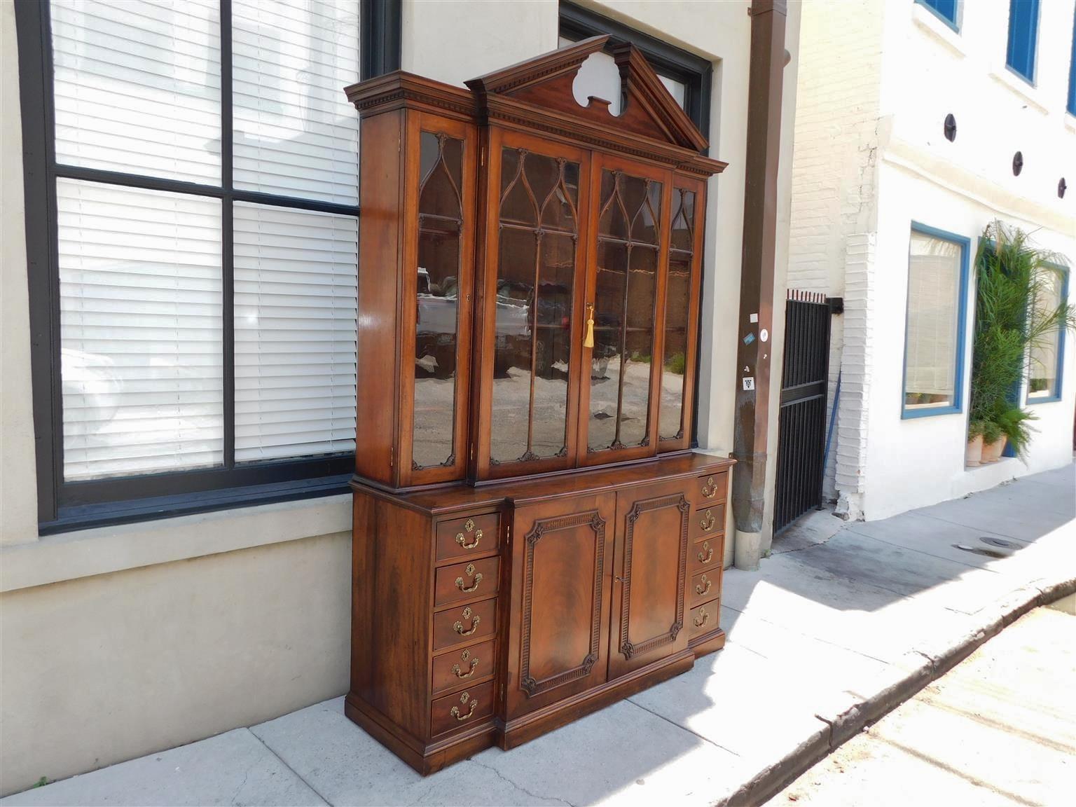 English Chippendale mahogany breakfront / bookcase with a broken arch pediment dentil molding cornice, flanking upper case hinged glass doors with decorative foliage mullions and adjustable interior shelving, flanking lower case hinged book matched
