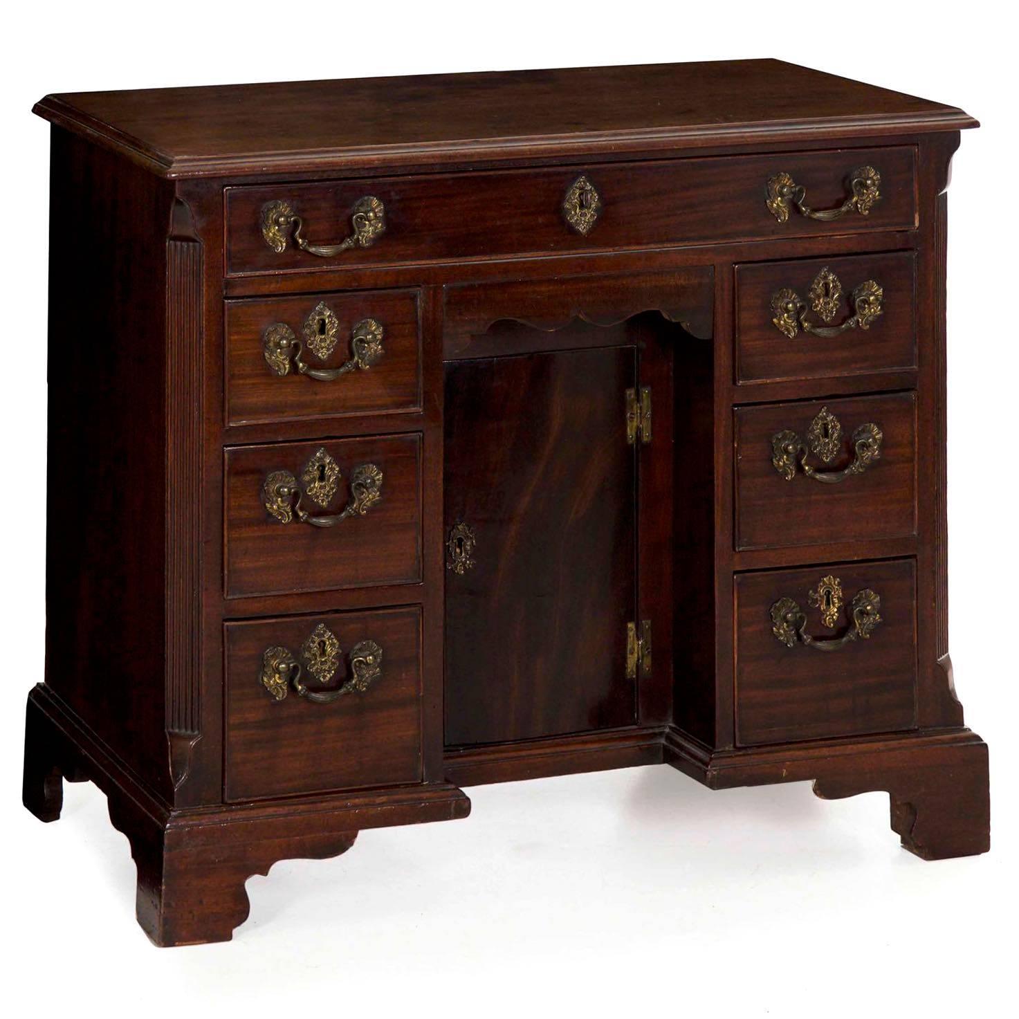 With a diminutive and restrained profile, this fine George II period kneehole desk is characterized by a single full width frieze drawer over a hidden centre drawer with “cupid’s bow” scalloping over a prospect door set back into the case. This is