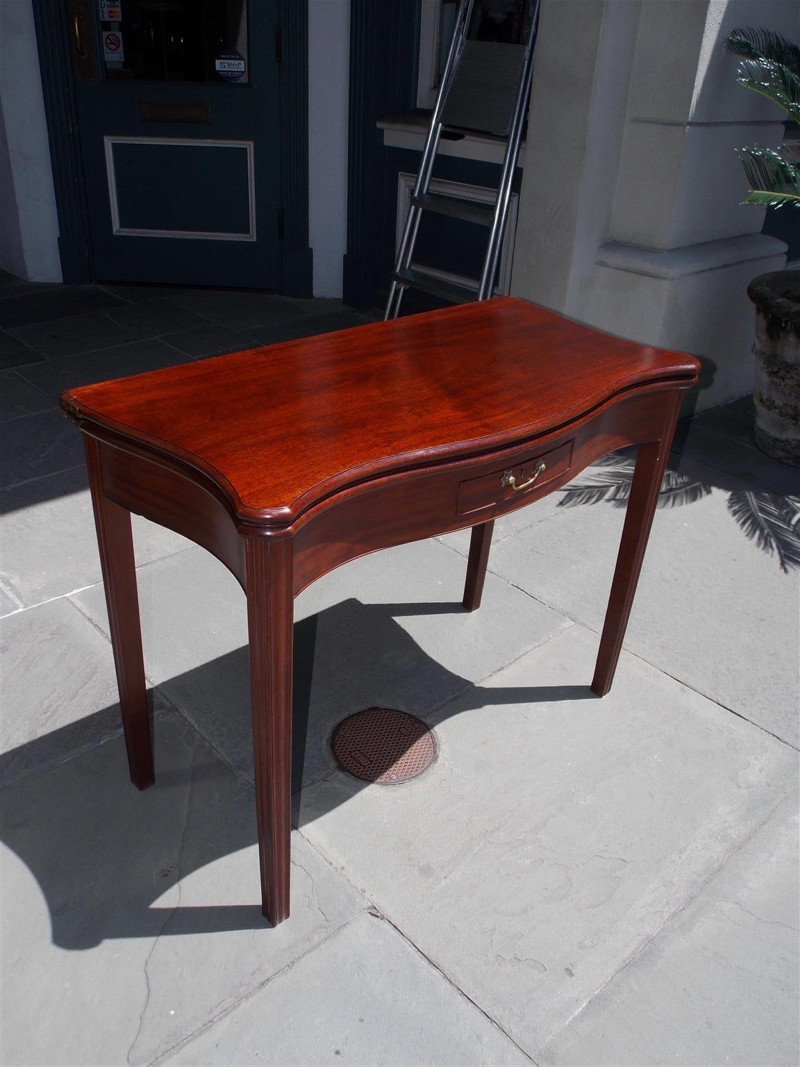 English Chippendale mahogany serpentine hinged game table with a one board top, centered drawer with the original brass, single rear gate leg, and terminating on the original carved molded tapered squared leg. Mid-18th century.