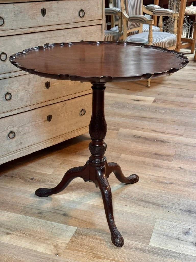 Mesa basculante inglesa de caoba Chippendale, S. XVIII.  Mesa basculante de época Jorge III finamente tallada en rica caoba, hacia 1760. El borde festoneado de la corteza remata un pedestal torneado y estriado con patas talladas en acanto que