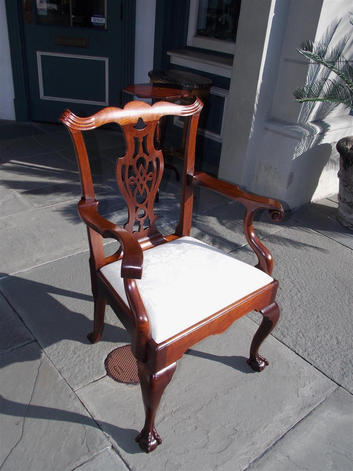 English Chippendale Mahogany upholstered arm chair with serpentine crest, fluted scrolled ears, intricately carved splat back, curvature scrolled arms, removable white muslin seat, scalloped skirt, and resting on carved knees with ball and claw