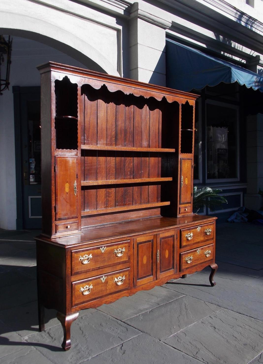 English Chippendale oak welsh dresser with a carved molded scalloped cornice, upper case with decorative carved flanking shelves, hinged cabinet doors cross banded with walnut and satinwood diamond thistle inlays revealing interior shelves, three