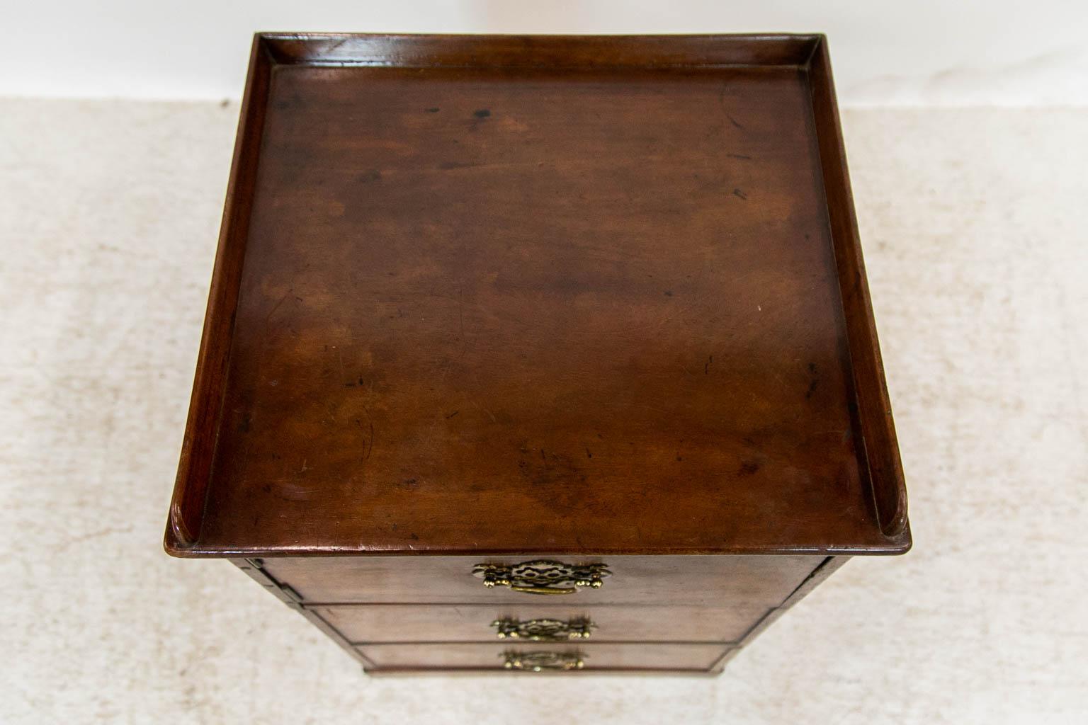 He upper most compartment of this small chest/cabinet has a door that opens to expose the interior. The lower two are working drawers. The top has a gallery on three sides. The hardware is later. This piece could have been converted possibly from a