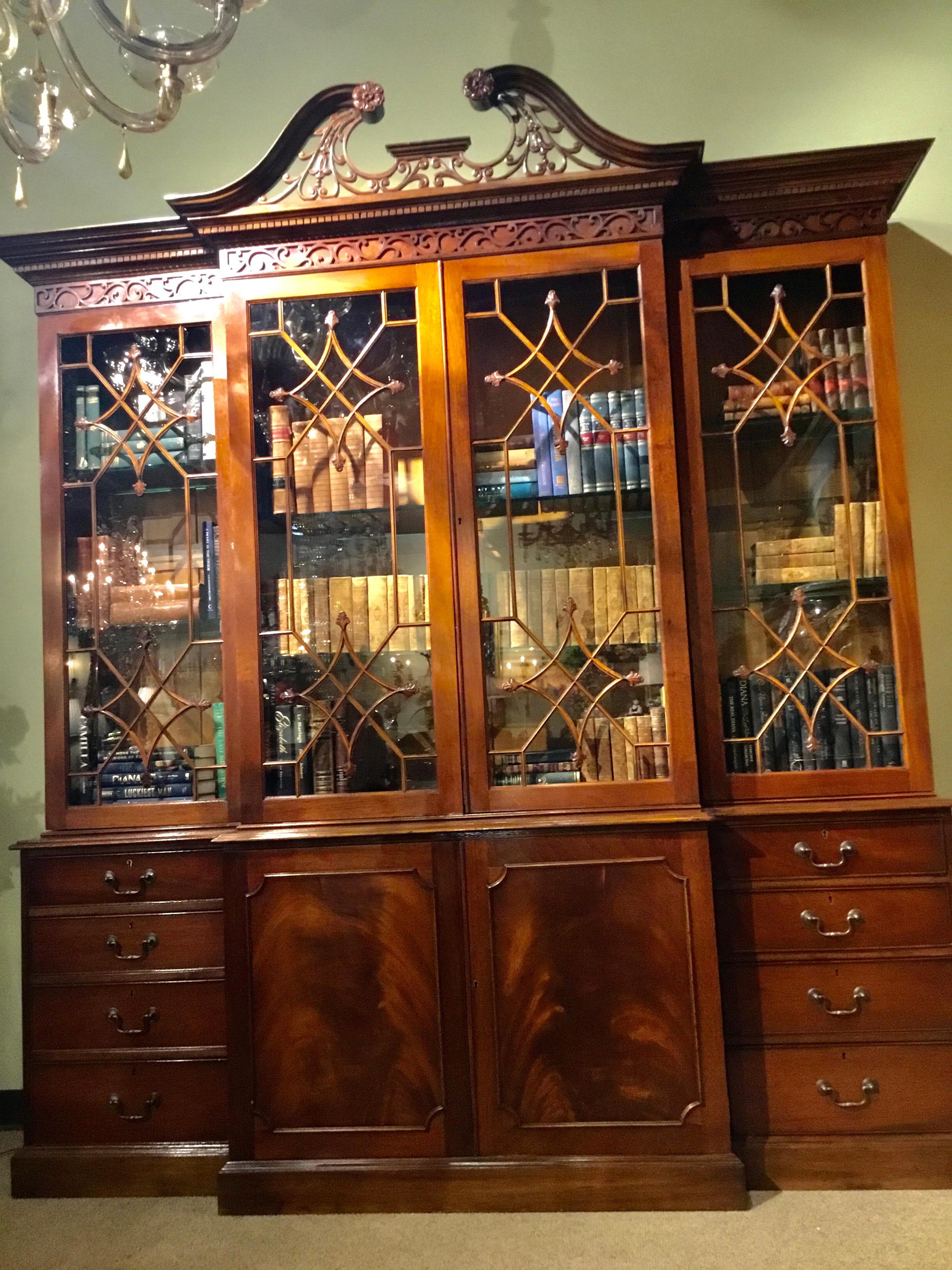 Handsome Chippendale style breakfront/ bookcase crafted of flame mahogany
with a superb swans neck and filigree pediment. The dentil cornice atop a carved
Blind-fret frieze and glazed doors with shaped astragal moldings having carved
fleur-de-lis