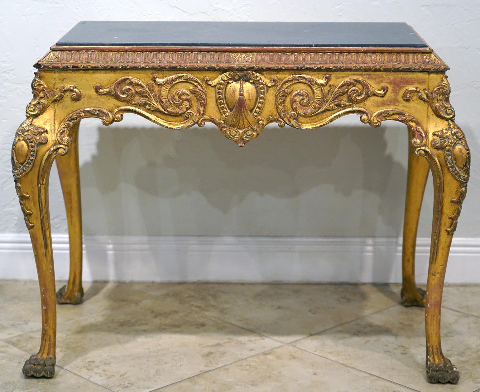 This English Chippendale style carved gilt wood table features a recessed marble top above delicately detailed aprons with scrolled leaf work centering medallions resting on four bold and equally detailed cabriole legs ending in carved paw feet.