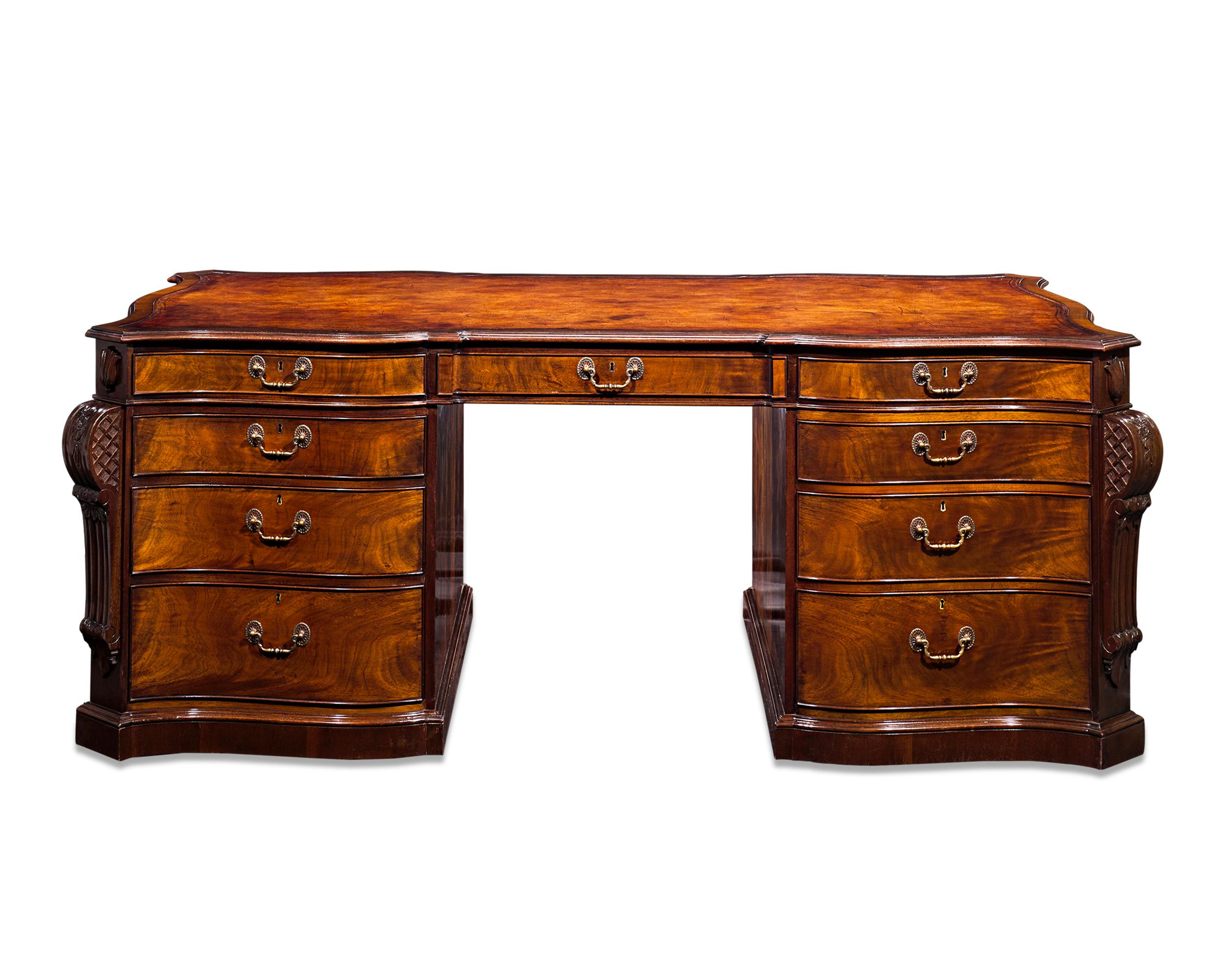 This extraordinary antique mahogany partner’s desk features a graceful serpentine form synonymous with the Rococo design pioneered by the famed Thomas Chippendale. Incorporating expertly carved molding and panelling on all sides, the desk is