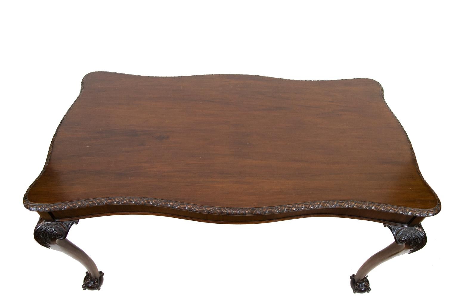 English Chippendale style table, the four serpentine shaped sides with repeating floral and ribbon top molding. The cabriole legs are carved with acanthus leaves and volutes terminating in large ball and claw feet. The apron is banded with figured