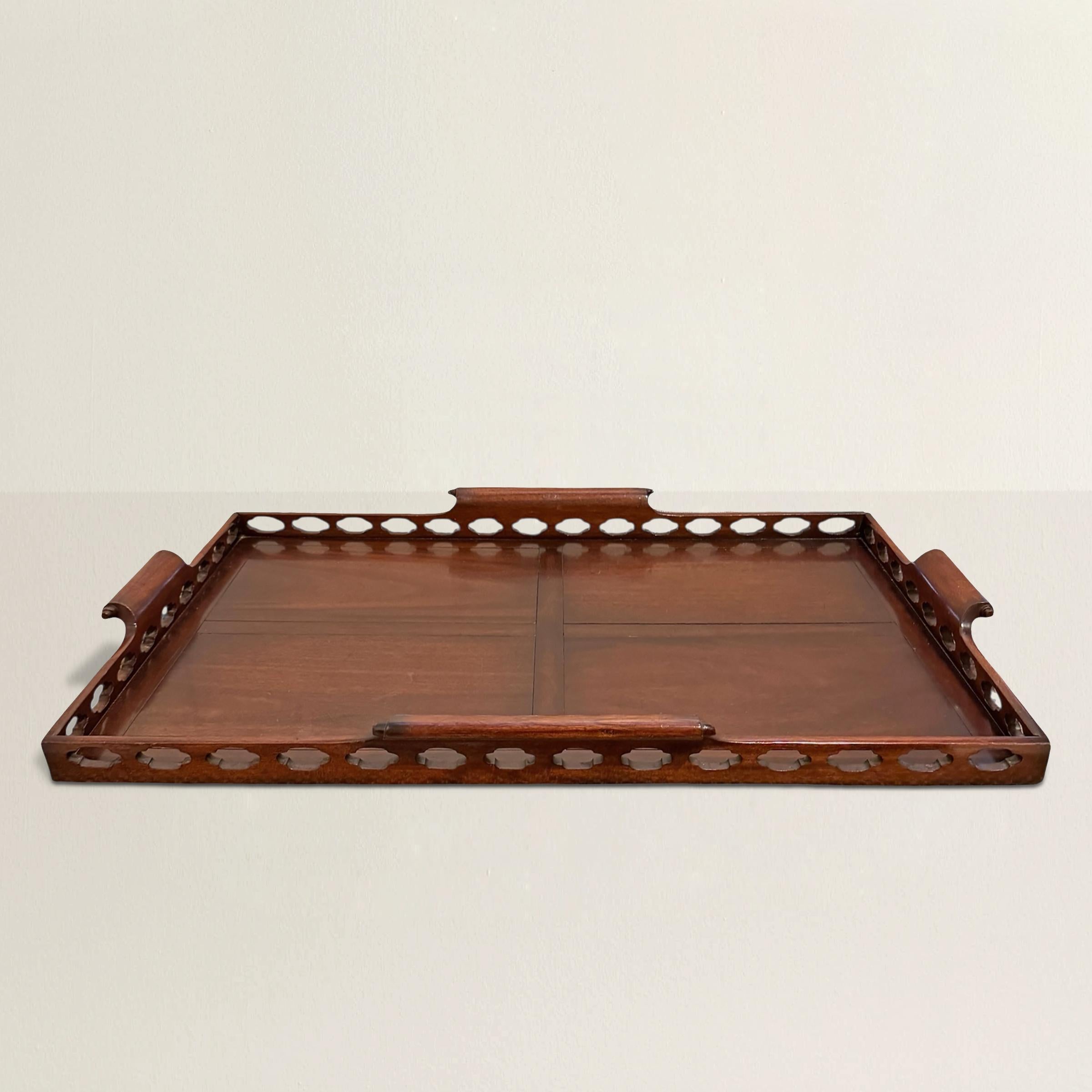Bold in scale and rich with detail, this English 20th-century Chippendale-style butler’s tray is anything but background. Crafted from mahogany, it features a pierced quatrefoil gallery that wraps the perimeter like a fine lace—refined, but not