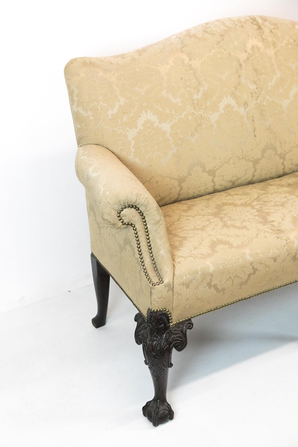 English Chippendale style upholstered settee, with serpentine shaped back and nicely curved arms, this settee is covered with brass studded damask. It has acanthus carved legs terminating in ball and claw feet.