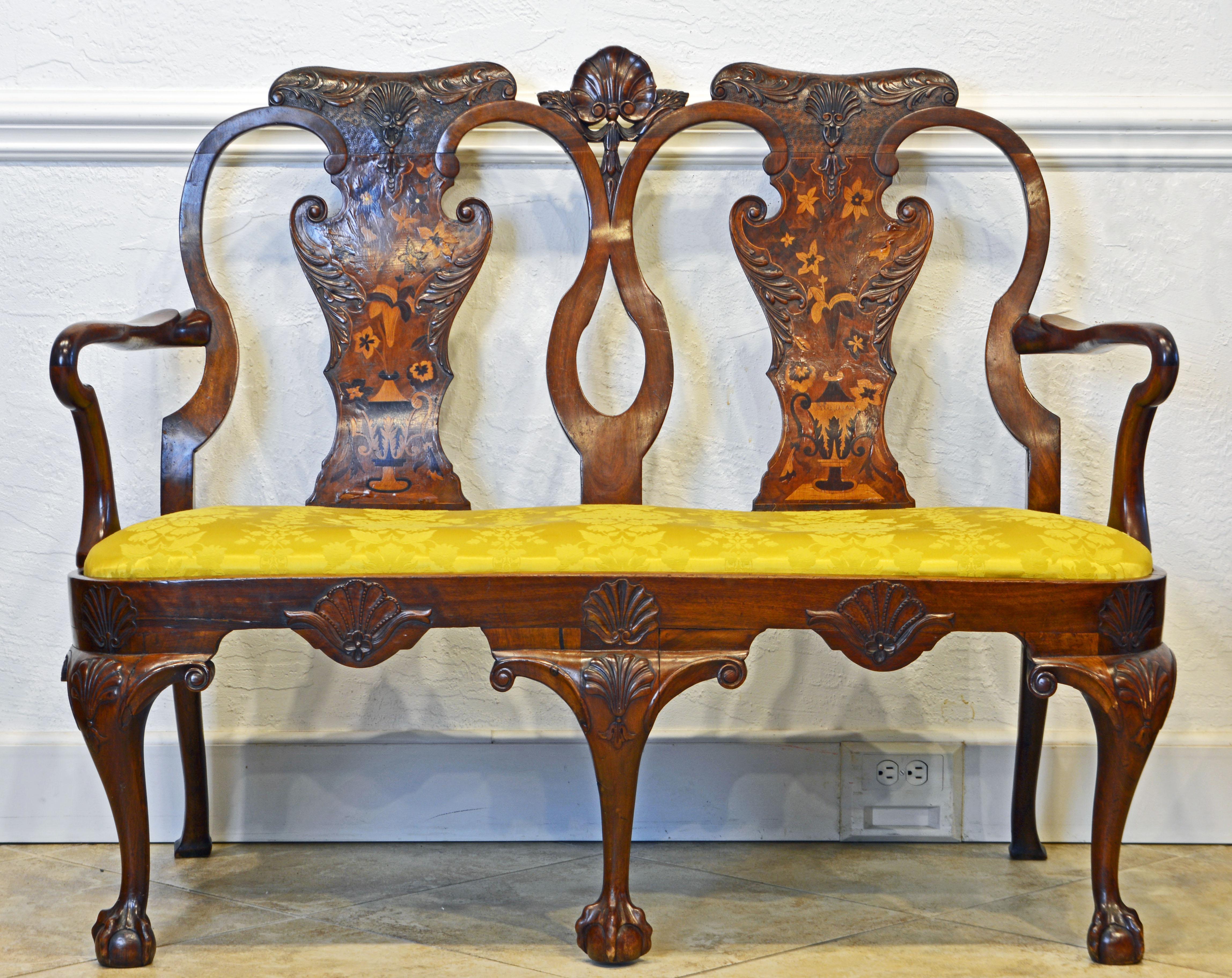 This English Chippendale style settee dates to the late 1900s and features an elegantly shaped frame adorned by leaf and shell carvings as well as fine inlay with flowers and urns on the back splats. It rests on three carved cabriole front legs