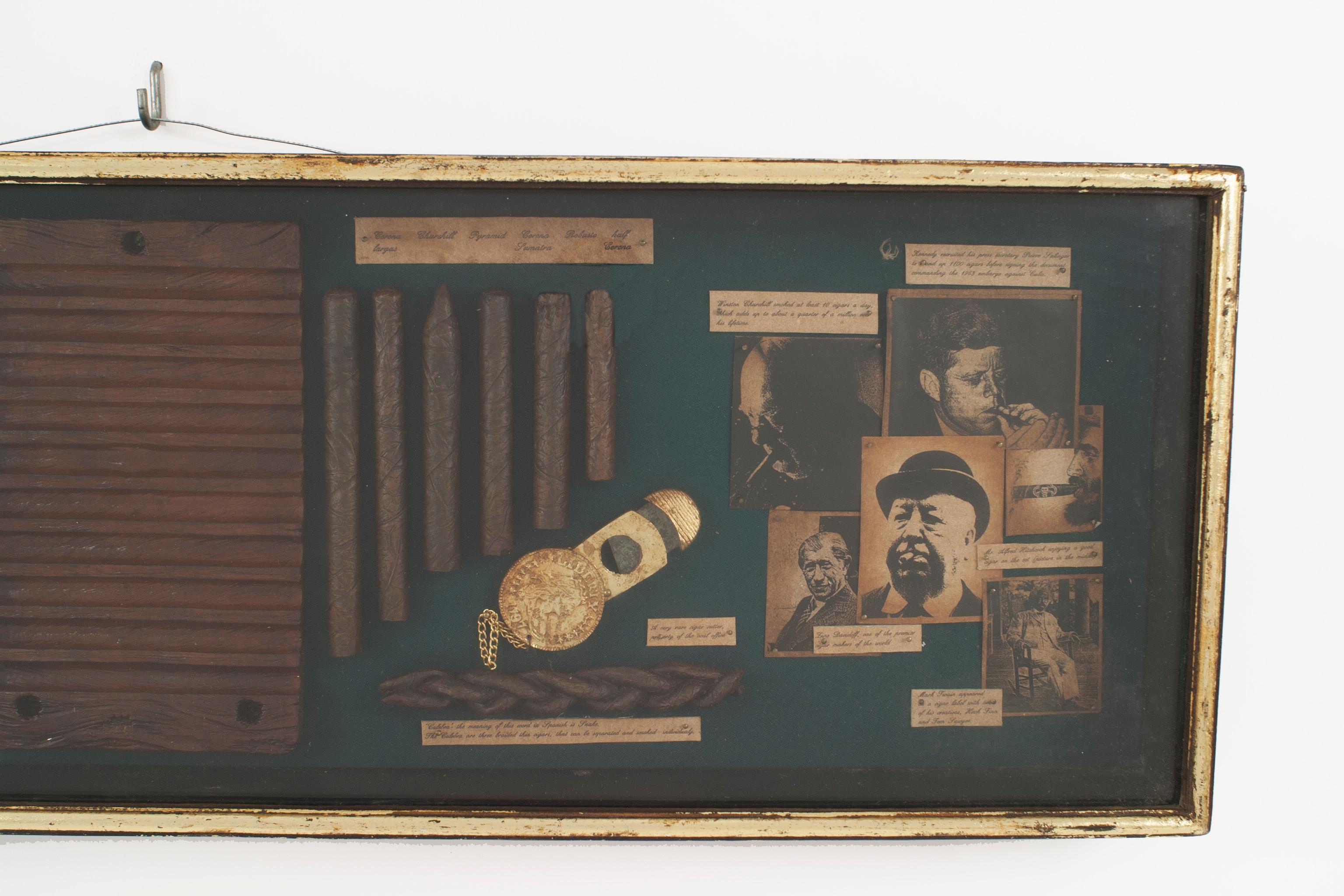 Vitrine/Wandtafel im englischen Stil mit Fotos berühmter Zigarrenraucher und Zigarrenzubehör auf grünem Filz hinter Glas