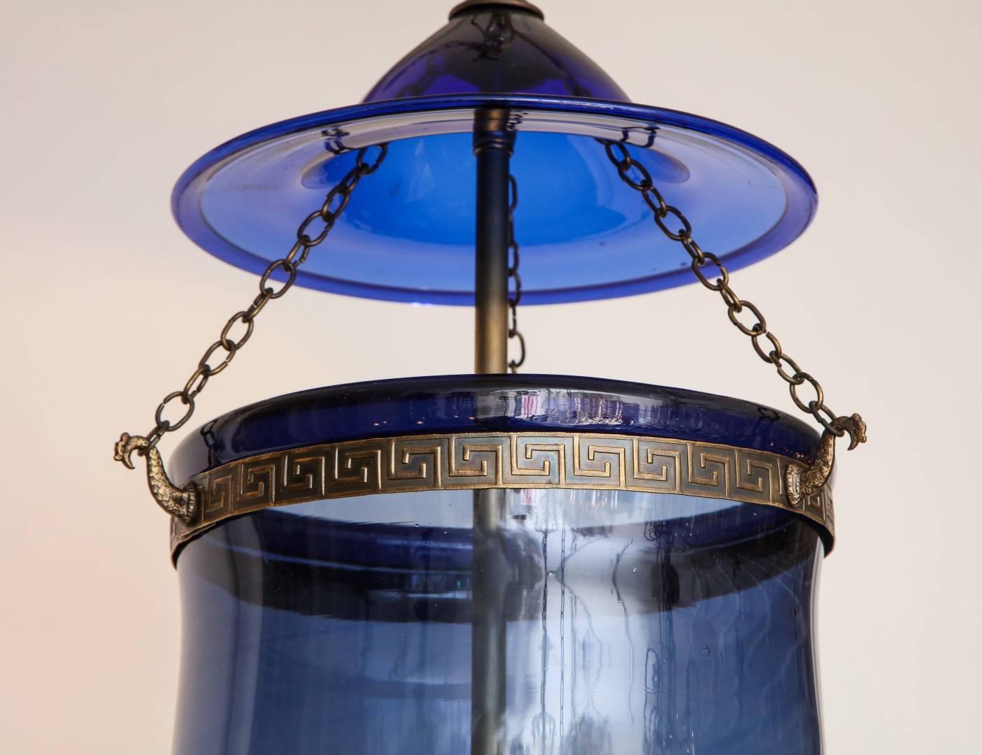 An English cobalt blue hanging glass lantern, suspending a tripartite candelabrum, with etched Greek key motif at collar, original smoke bell and brass fittings, 
New standard wiring 
Includes ceiling canopy and chain with matching antique brass
