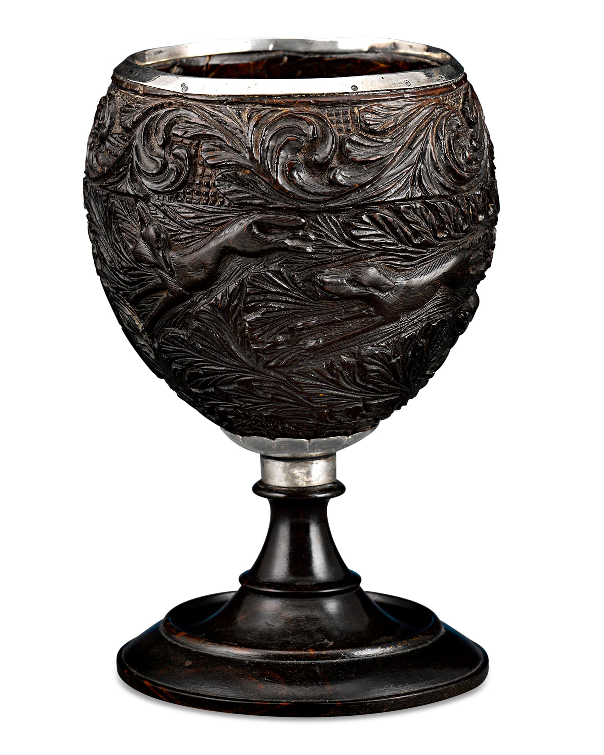 An exotic coconut fits perfectly into the ebony turned pedestal of this remarkably rare Georgian cup. Crafted during a period when coconuts were considered an extravagant novelty in England, this example bears highly detailed carvings that celebrate