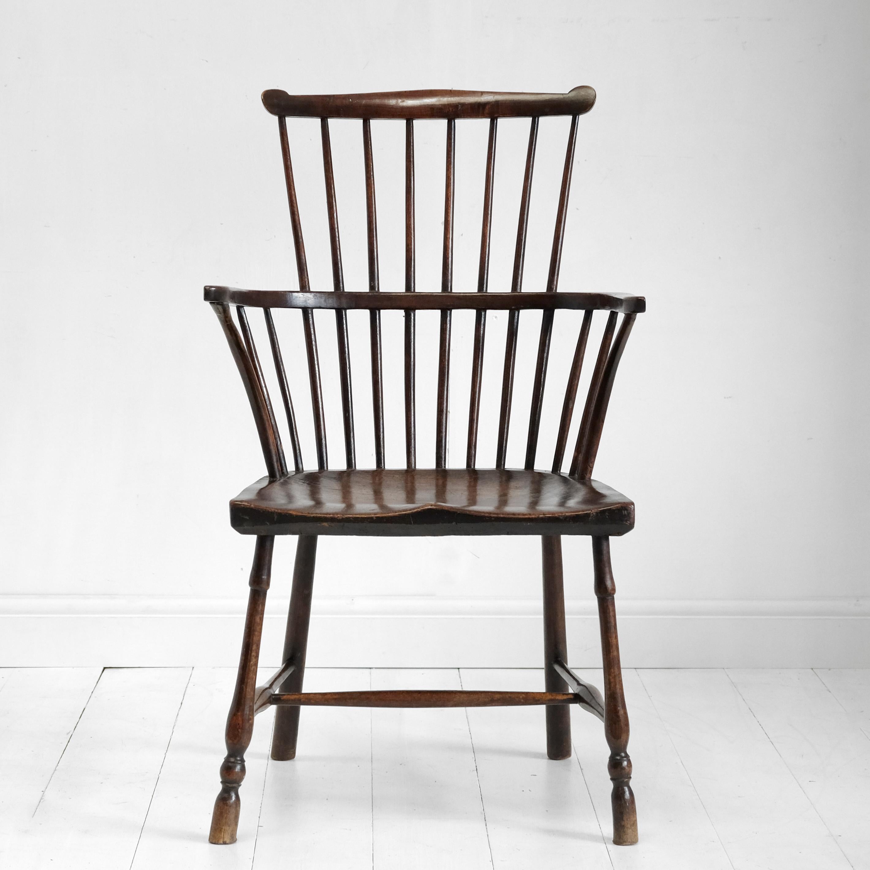 A comb back Windsor chair in elm and beech. Egg and reel turned front legs with plain tapered rear legs, united by a turned H-stretcher. Nicely shaped elm seat with pleasing color and grain pattern. The arm hoop with bent supports and simple stick